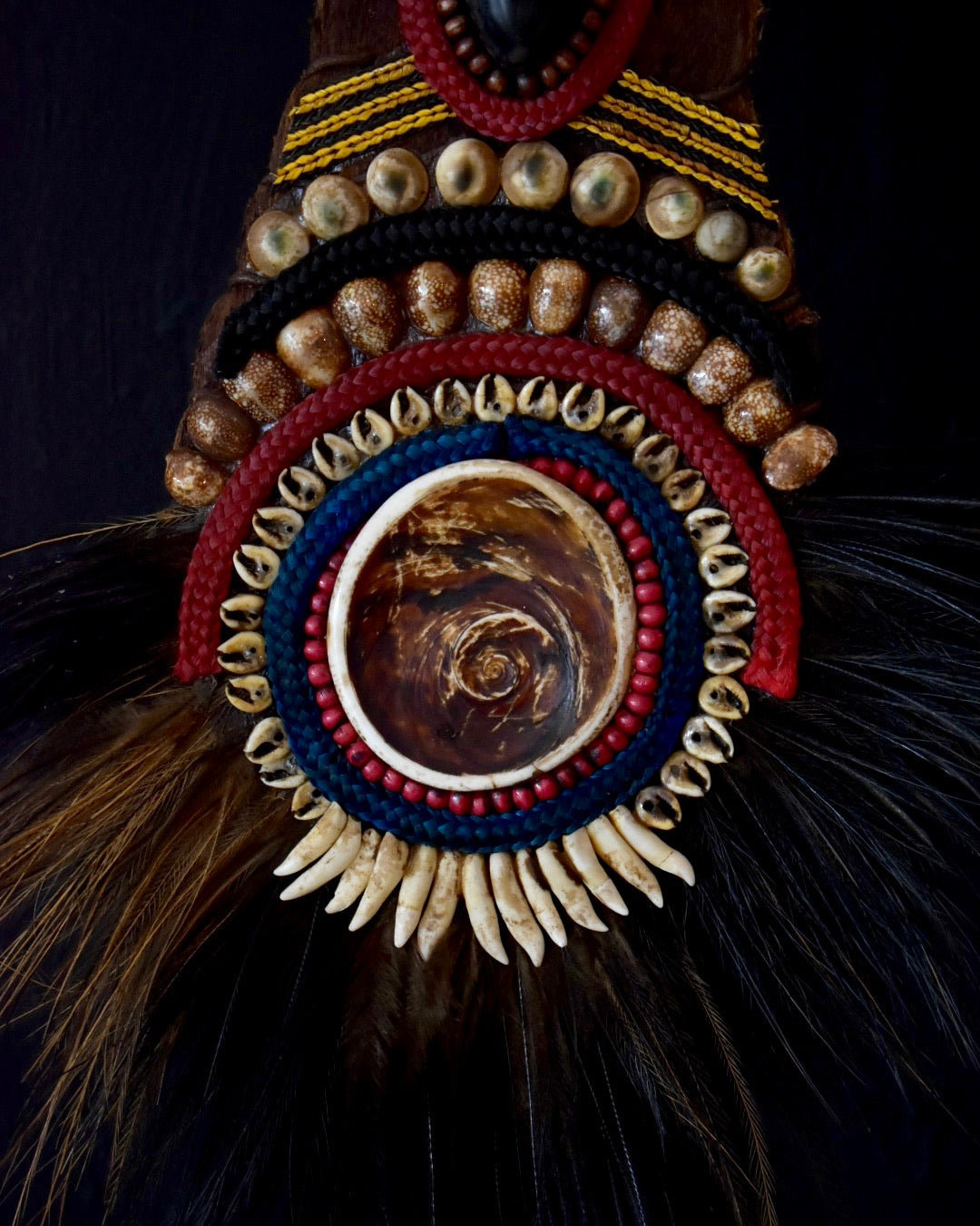 Decorative headdress with beads, feathers, and a central circular design on a dark background