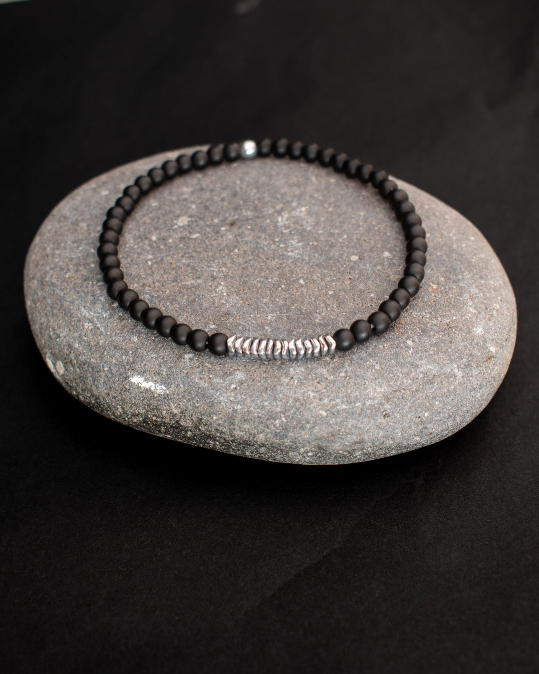 Black beaded bracelet with silver clasp on a gray stone against a black background