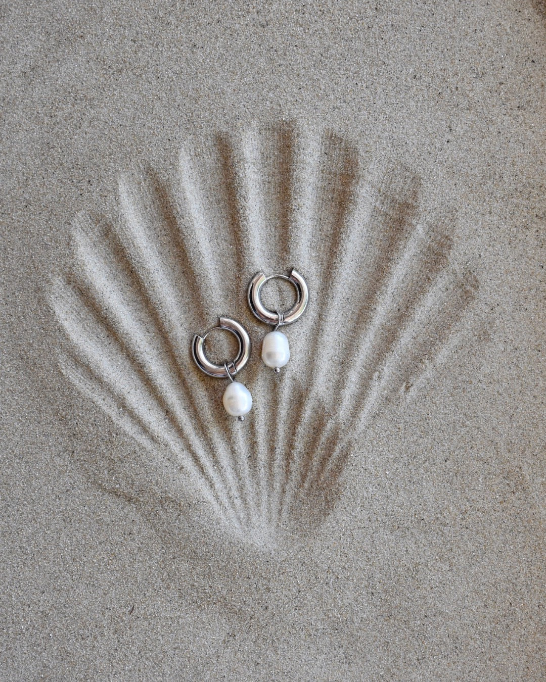 A pair of hoop earrings with fresh water pearls attached, placed on a ceramic plate with a wicker object in the background.