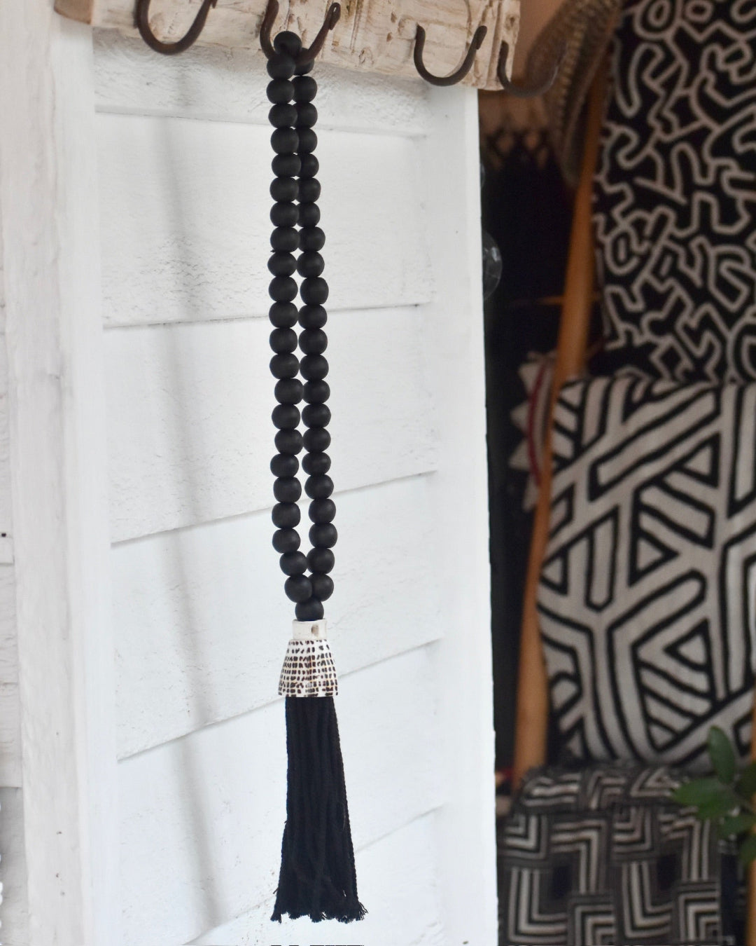 Black beaded necklace with a tassel hanging on a hook against a white wall.