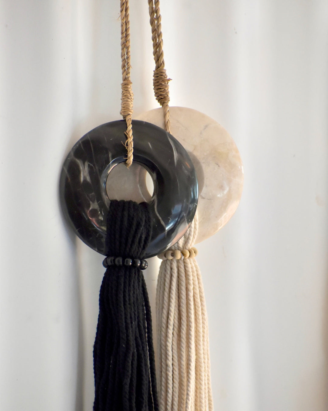 Decorative wall hanging with black and beige circular elements and tassels on a white background