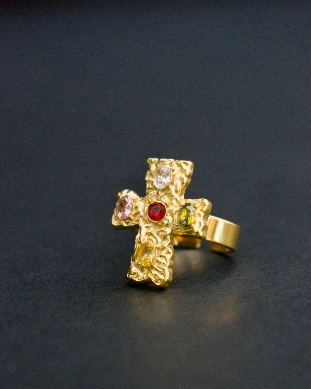 Gold cross-shaped earring with gemstones on a dark background