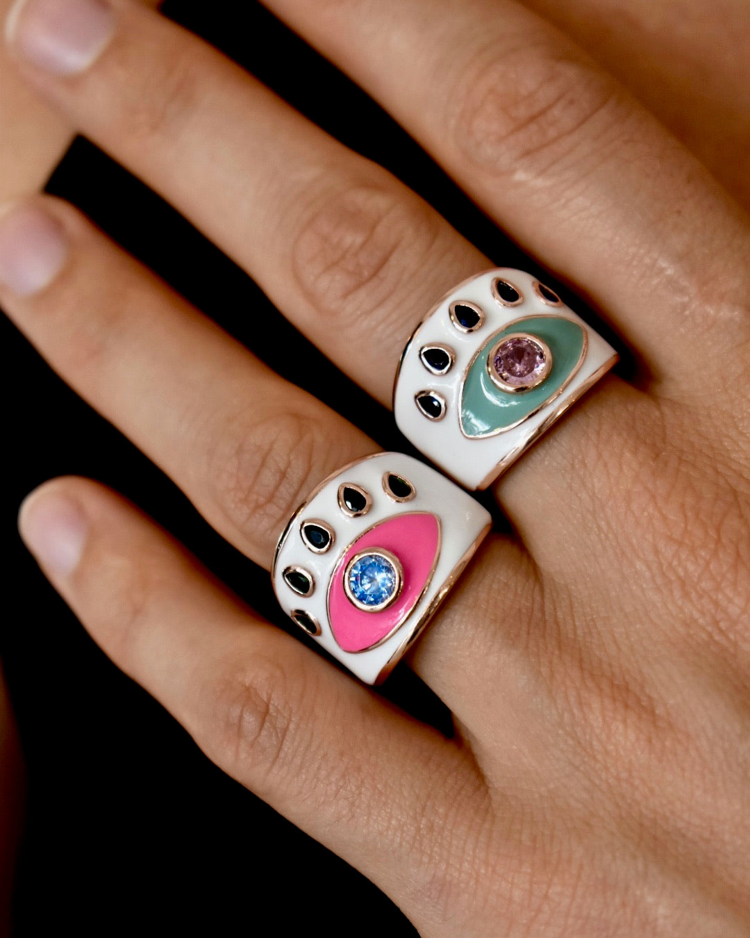Two paw-shaped rings with colorful gemstones on a hand against a dark background