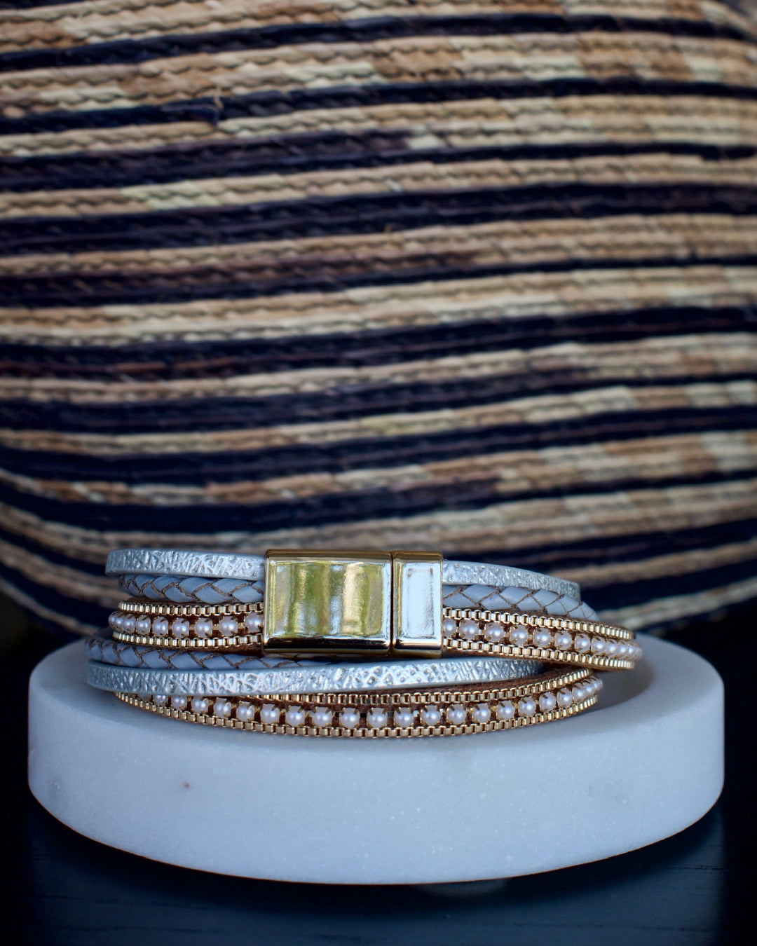 Set of three bracelets on a white cylindrical stand with a striped woven background