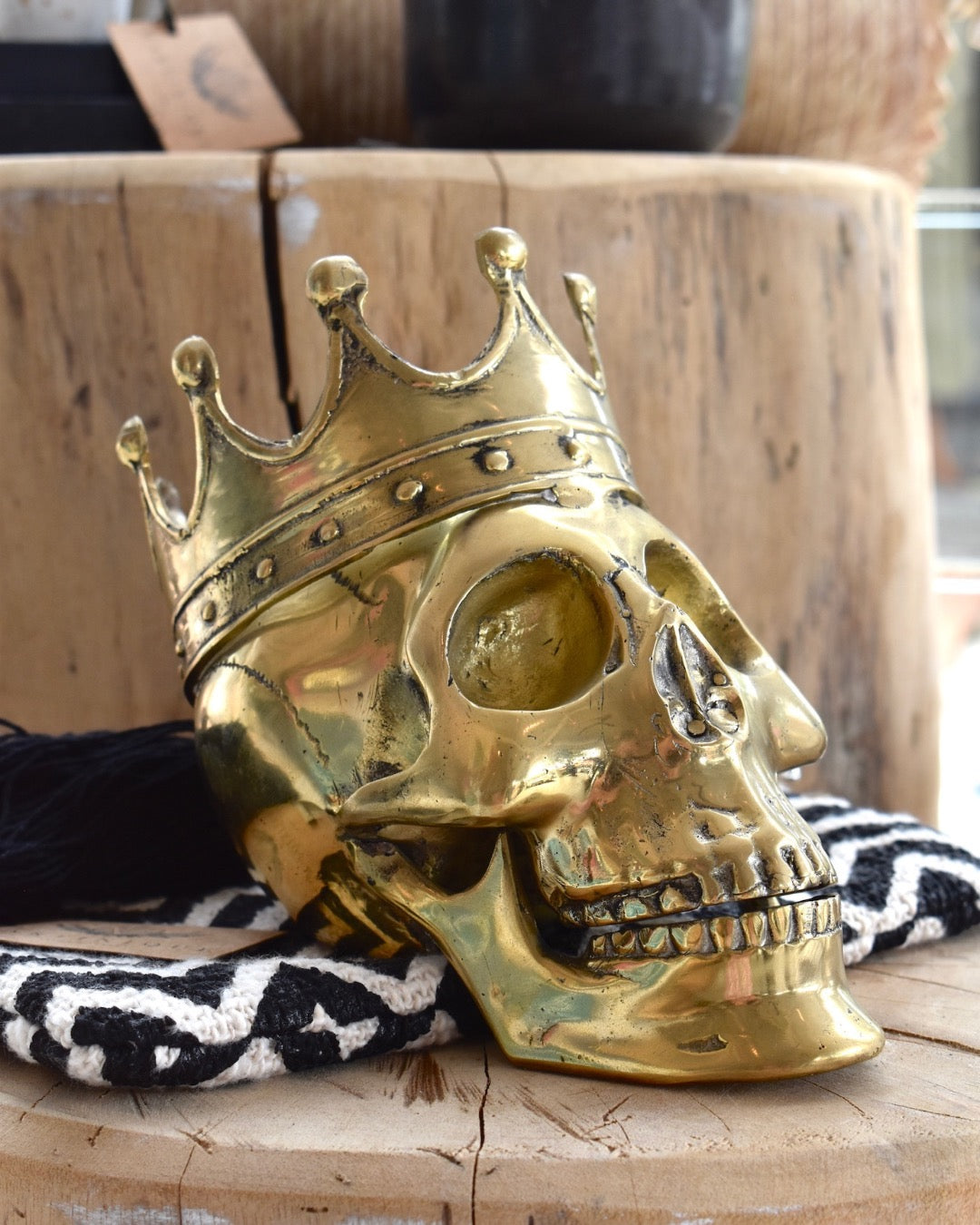 A gold brass skull with a decorative crown on top, placed on a wooden surface with a black and white striped fabric beside it.