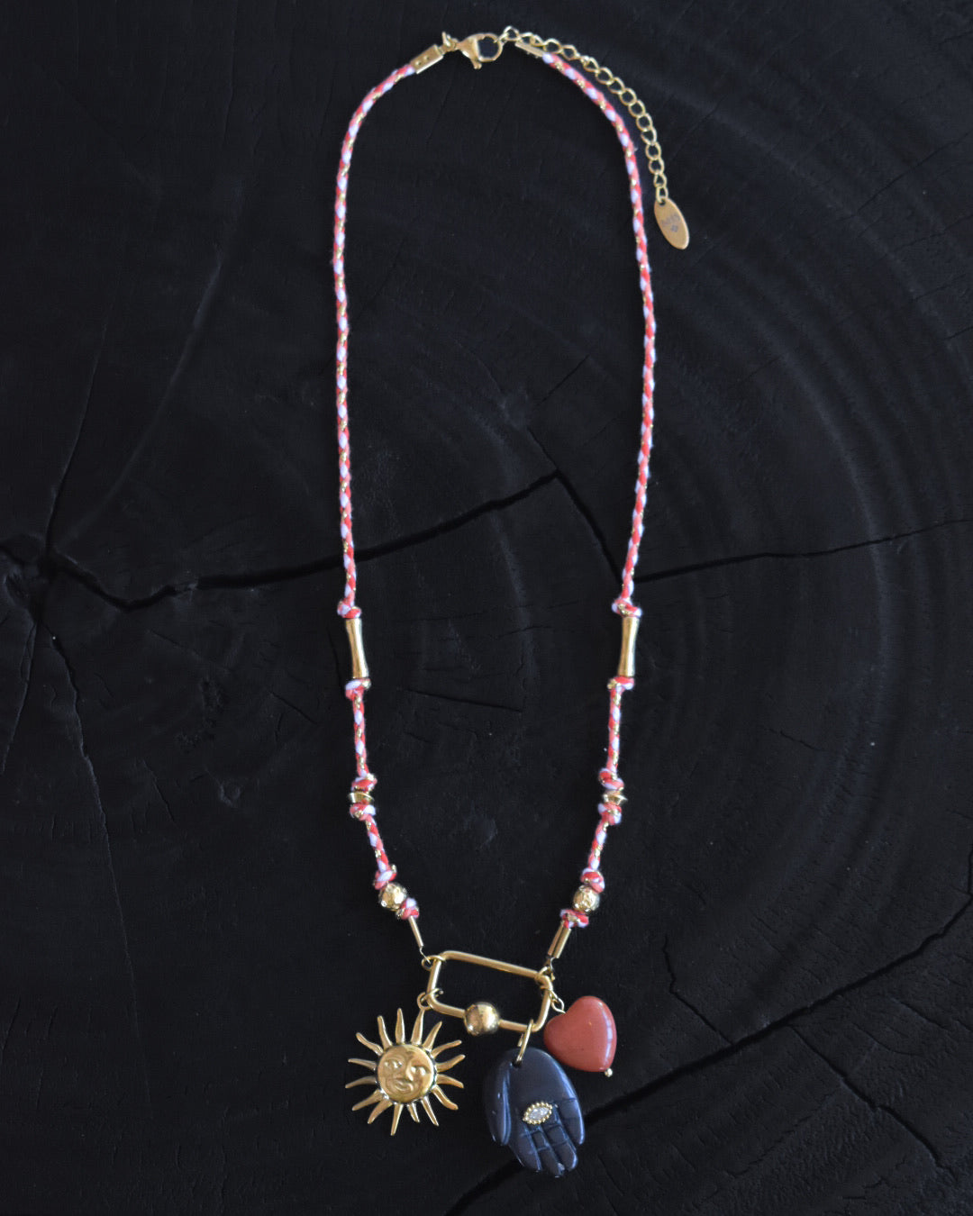 Necklace with sun, heart, and moon charms on a dark fabric background