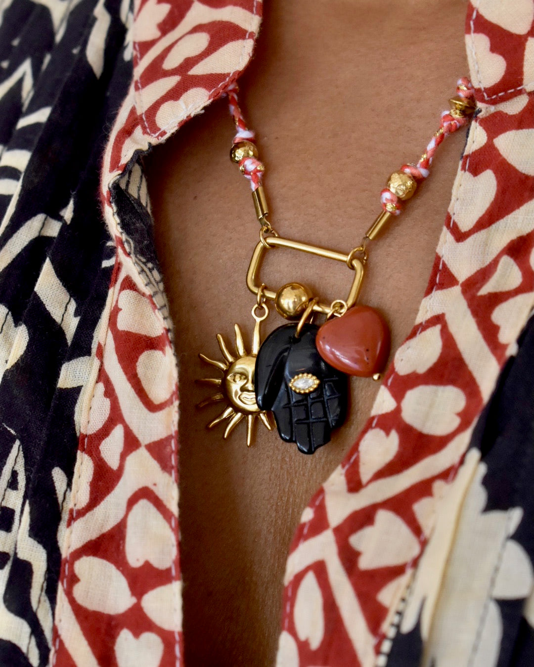 Necklace with sun, hand, and heart charms on a patterned shirt background