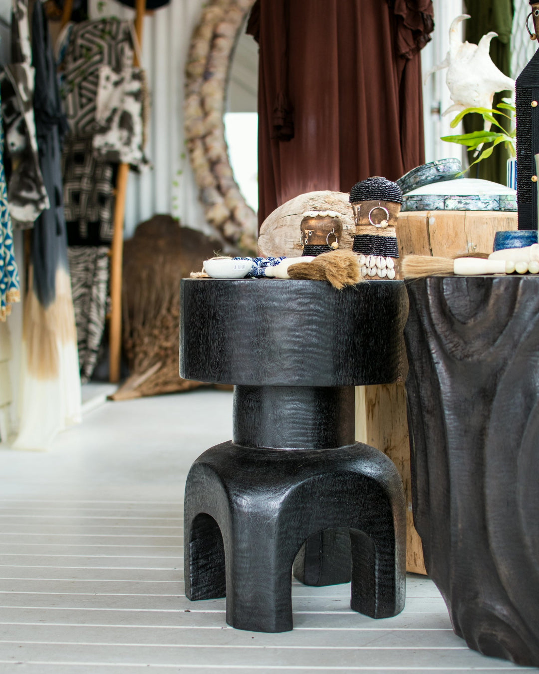 A dark carved wooden stool with a tiered design and curved legs, styled in a rustic, bohemian-themed room alongside other decorative items.