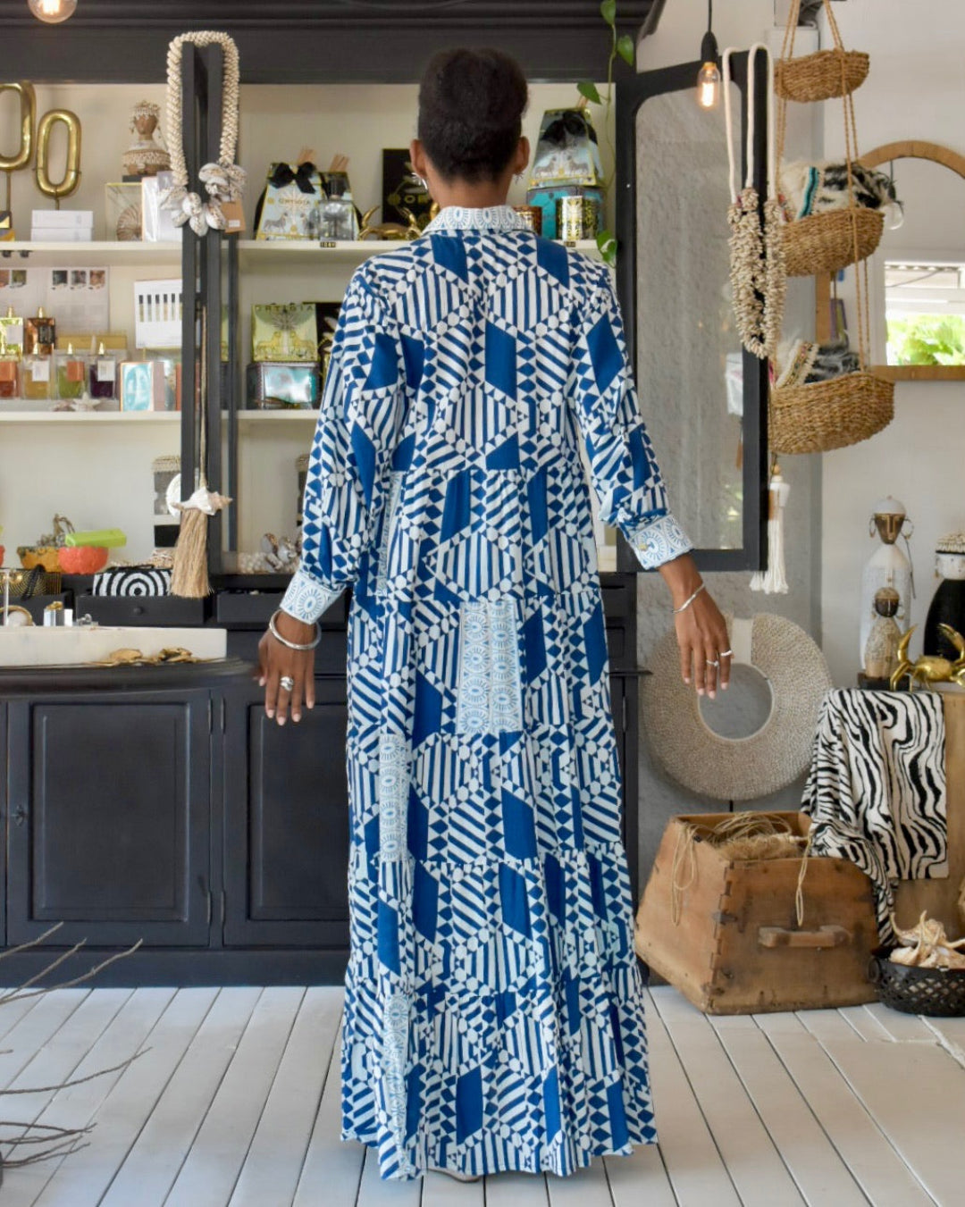 Woman in a blue and white patterned dress standing in a room with decor elements.