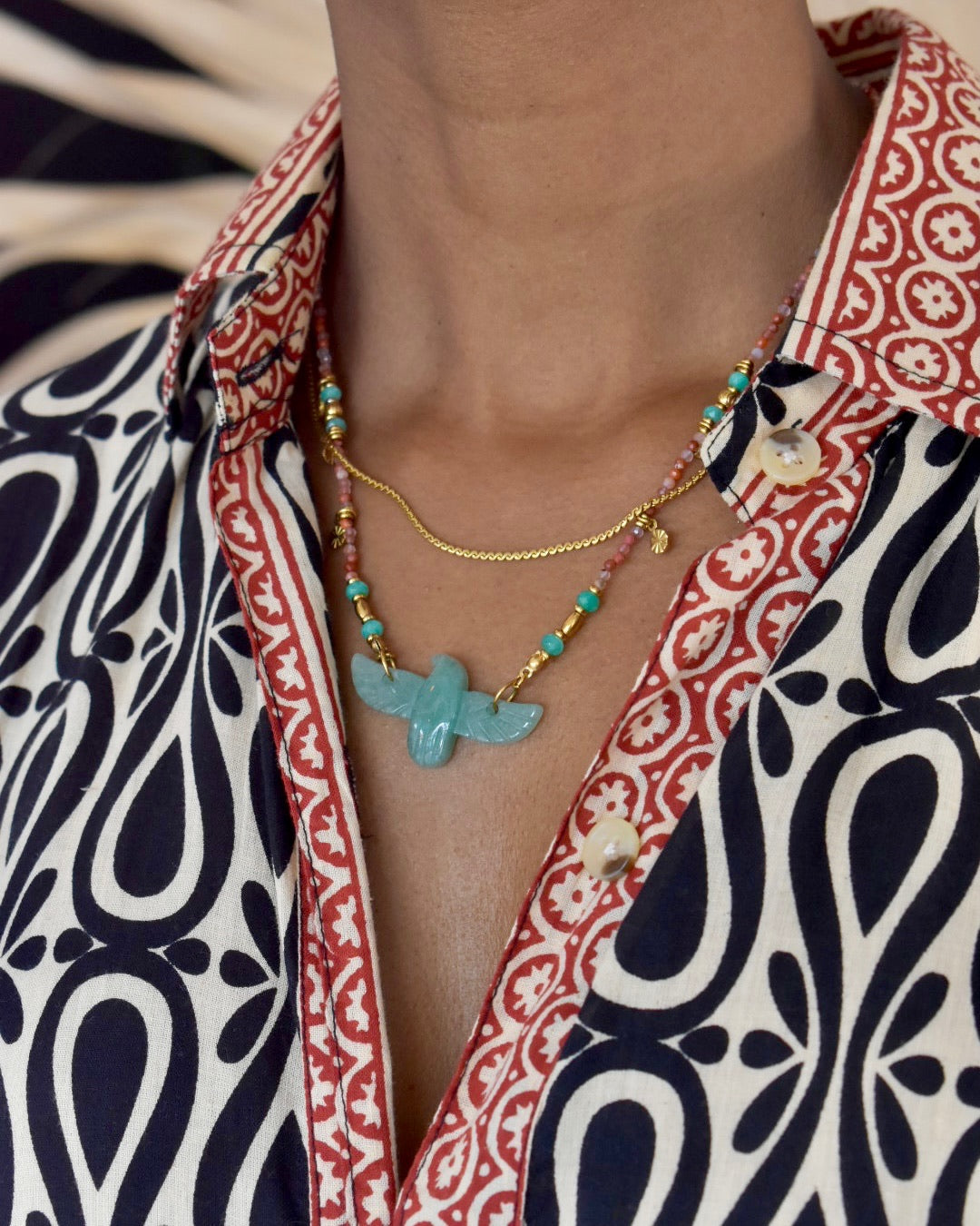 Necklace with a blue pendant worn by a person in a patterned shirt