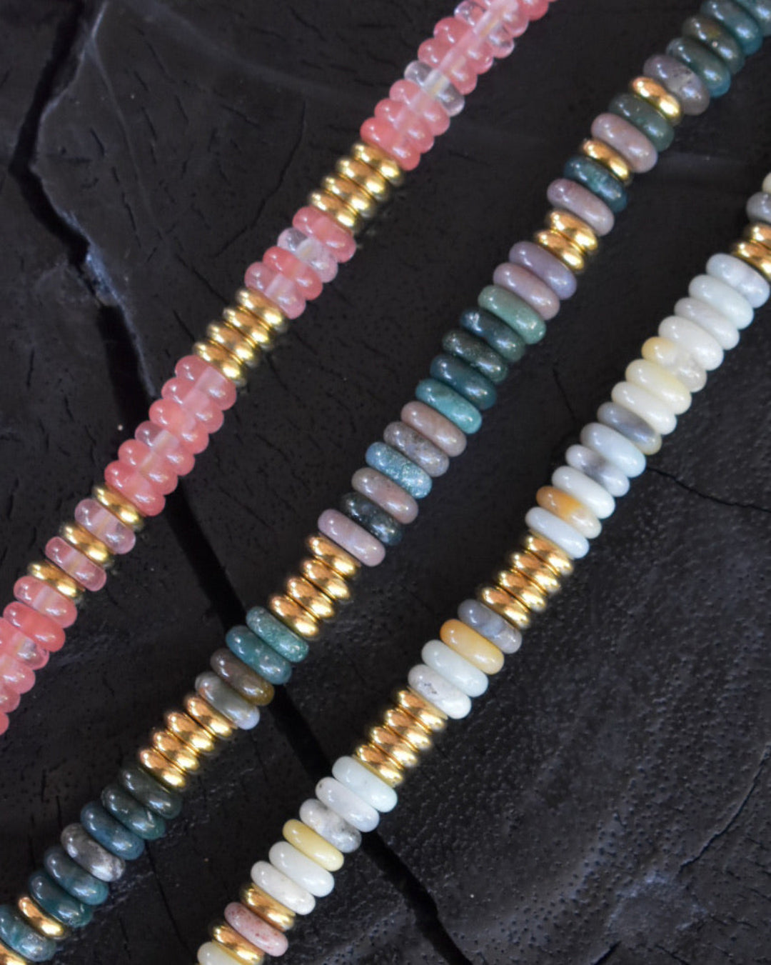 Beaded strands with pink, gold, blue, and white beads on a dark textured background