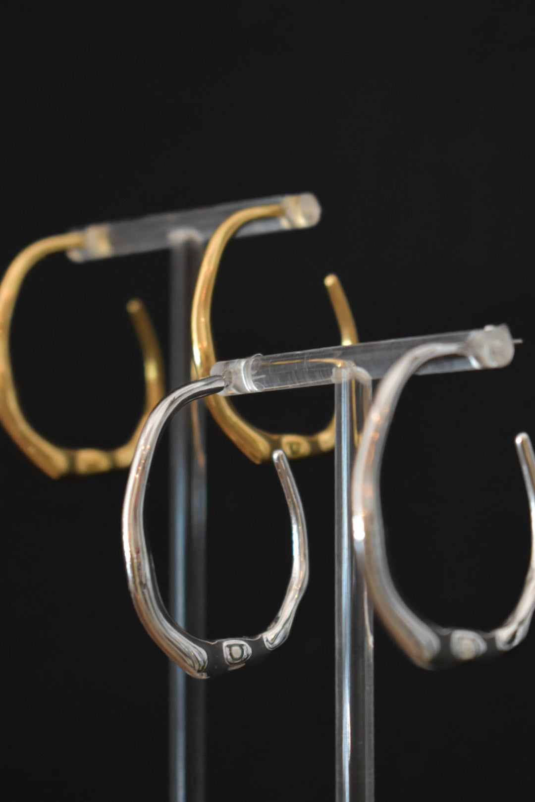 Pair of silver hoop earrings on a clear stand against a black background