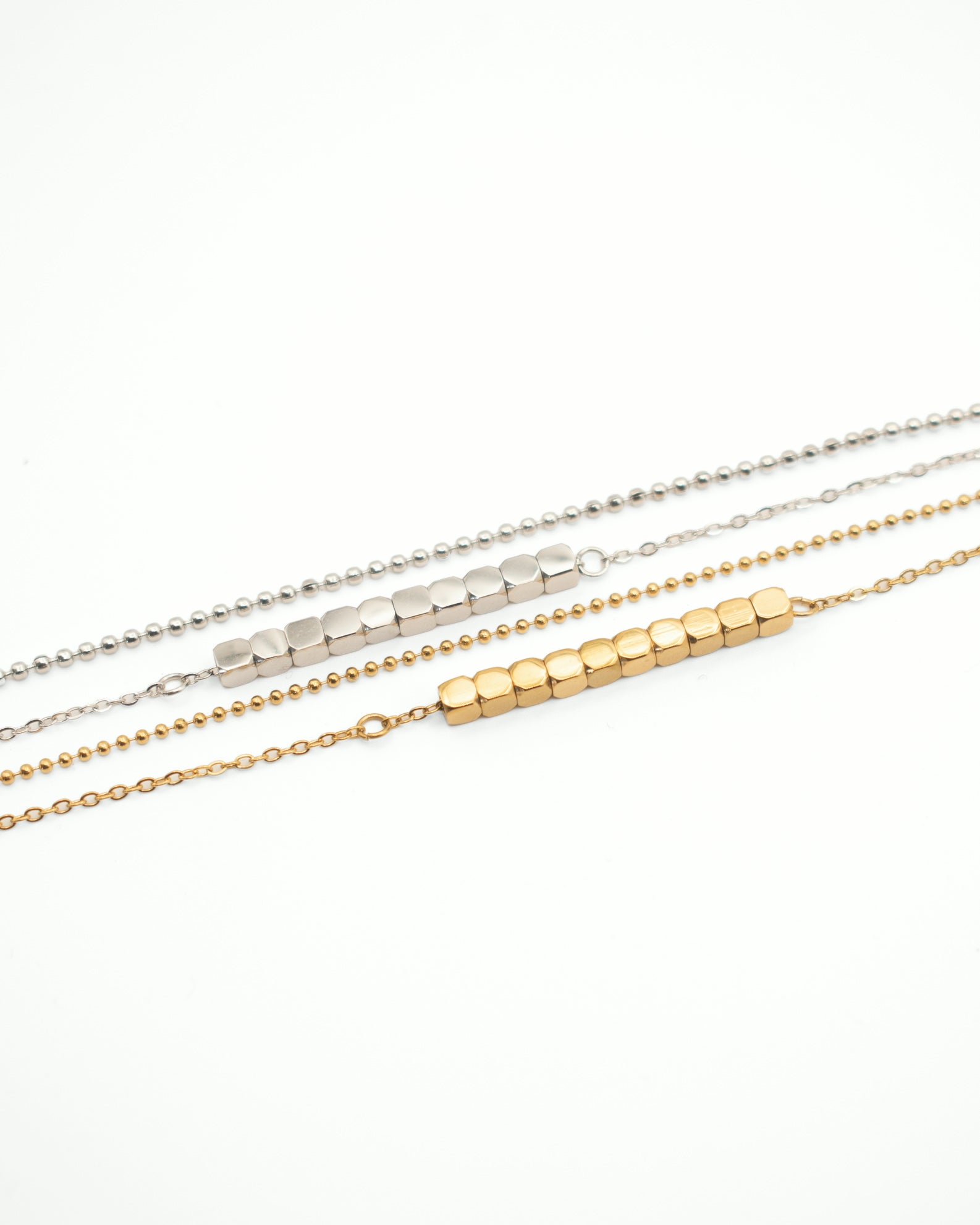 Three delicate bar necklaces laid parallel on a white background: one silver-tone, one two-tone silver-and-gold, and one gold-tone, each featuring a row of small cube-like beads on a fine chain.