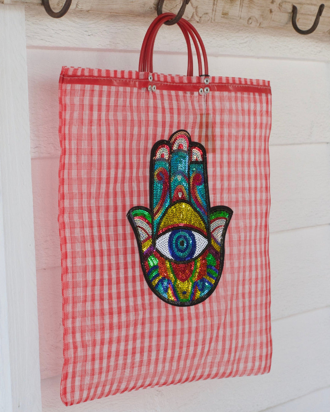 Red checkered tote bag with colorful Hamsa hand design on a wooden surface.