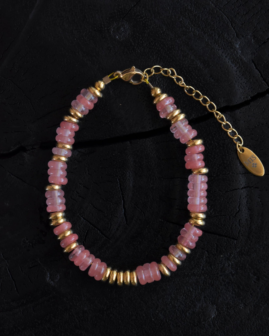 Bracelet with pink beads and gold accents on a dark background