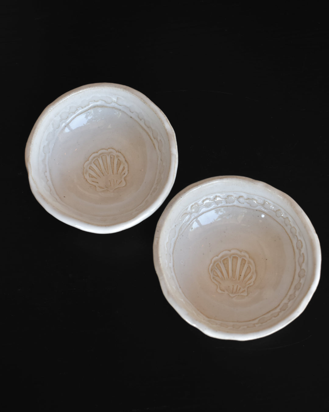 Two white ceramic bowls with shell design on a black background