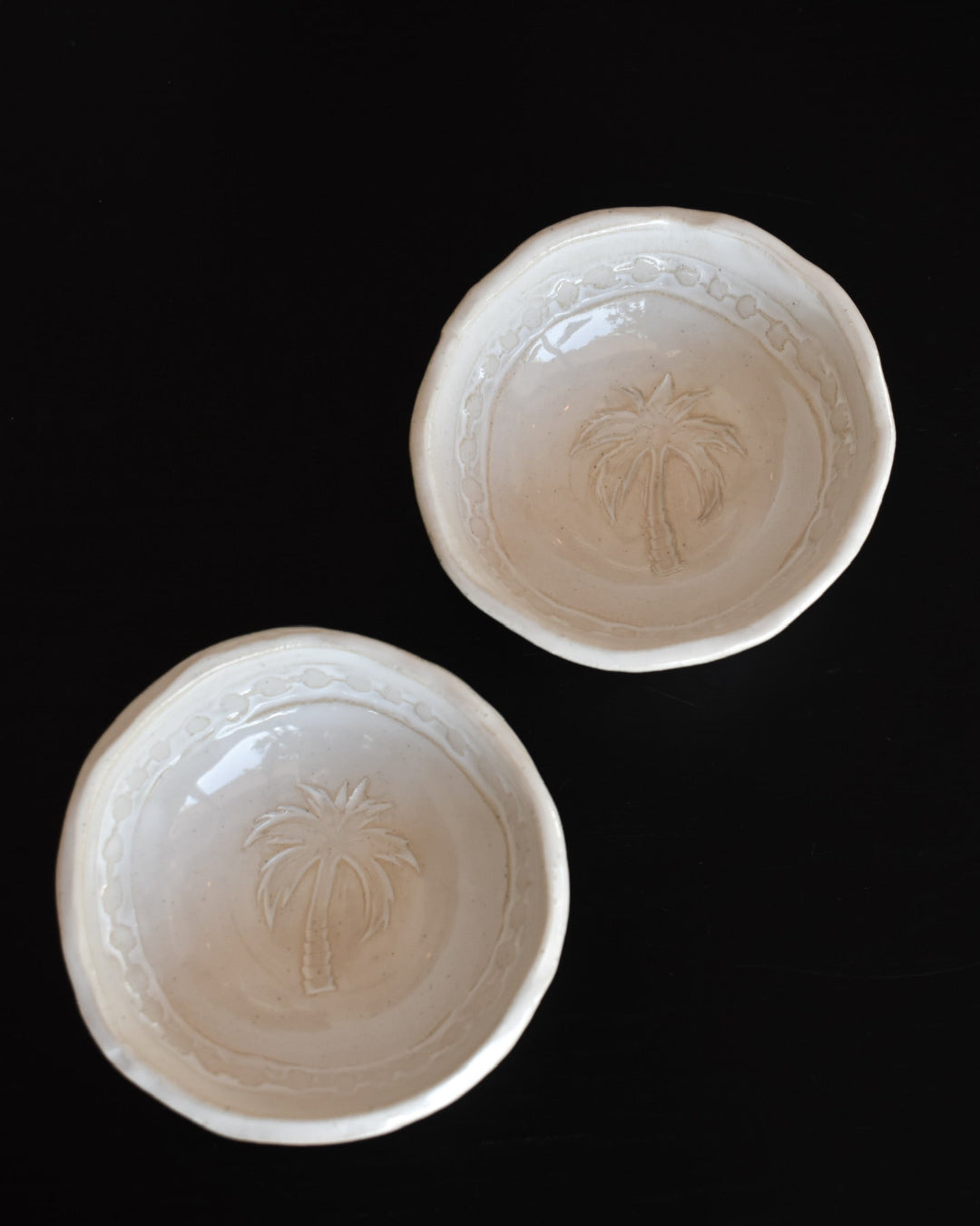 Two white ceramic bowls with palm tree design on a black background