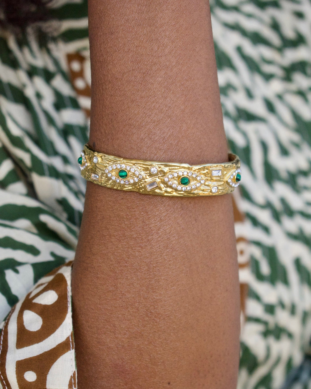 Gold bracelet with green stones on a wrist against a patterned fabric background