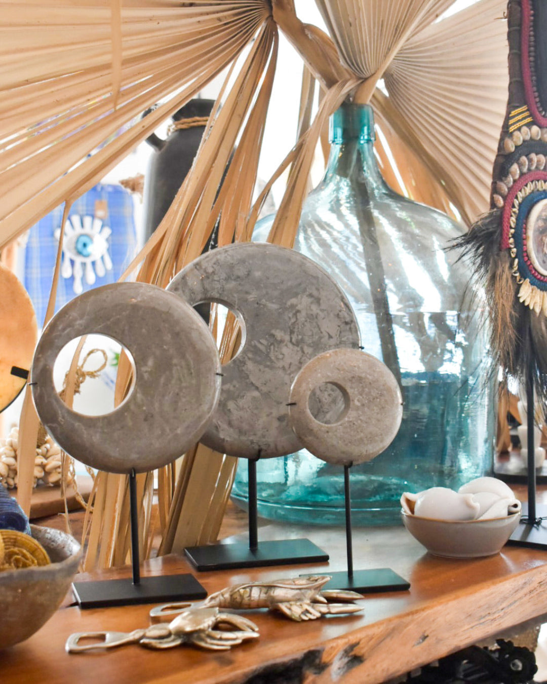 Decorative items including stone circles on stands, a large blue bottle, and dried palm leaves.