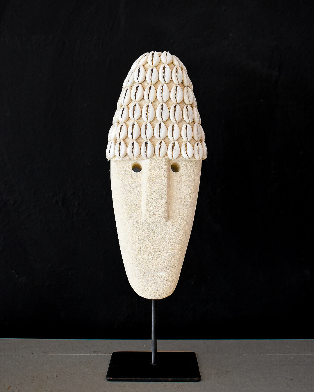 Decorative mask with shell-like top on a black stand against a black background