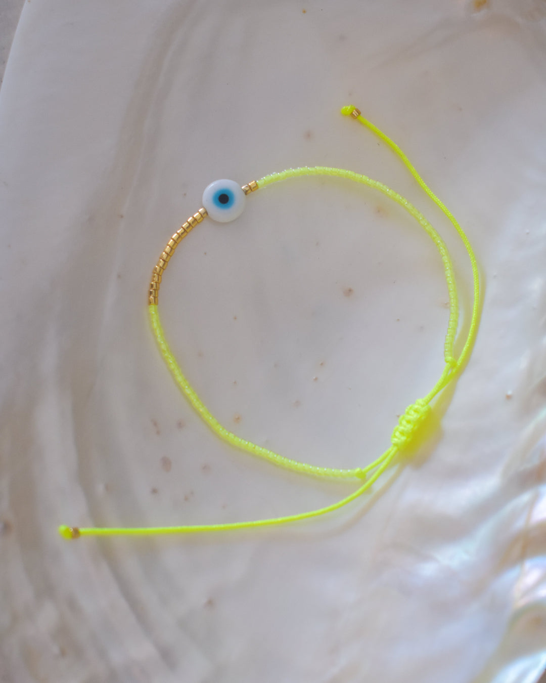 Yellow bracelet with a blue evil eye charm on a light beige background