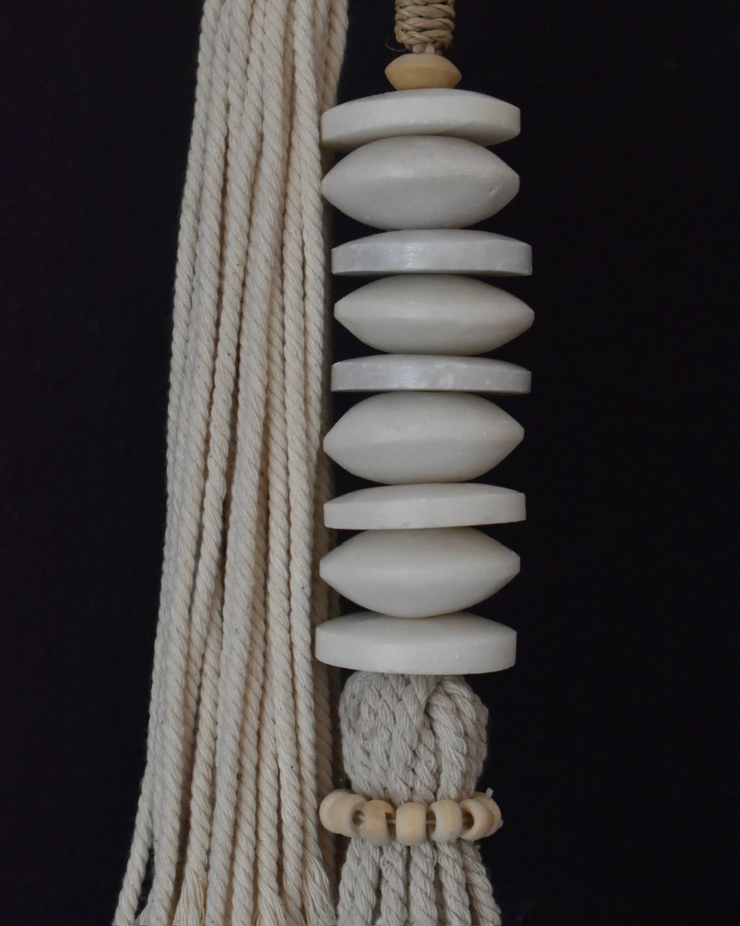 Decorative hanging with white marble beads and natural fibers on a black background
