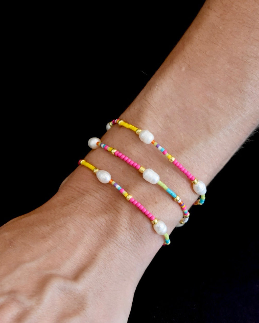 Multicolored beaded bracelet on a wrist against a black background