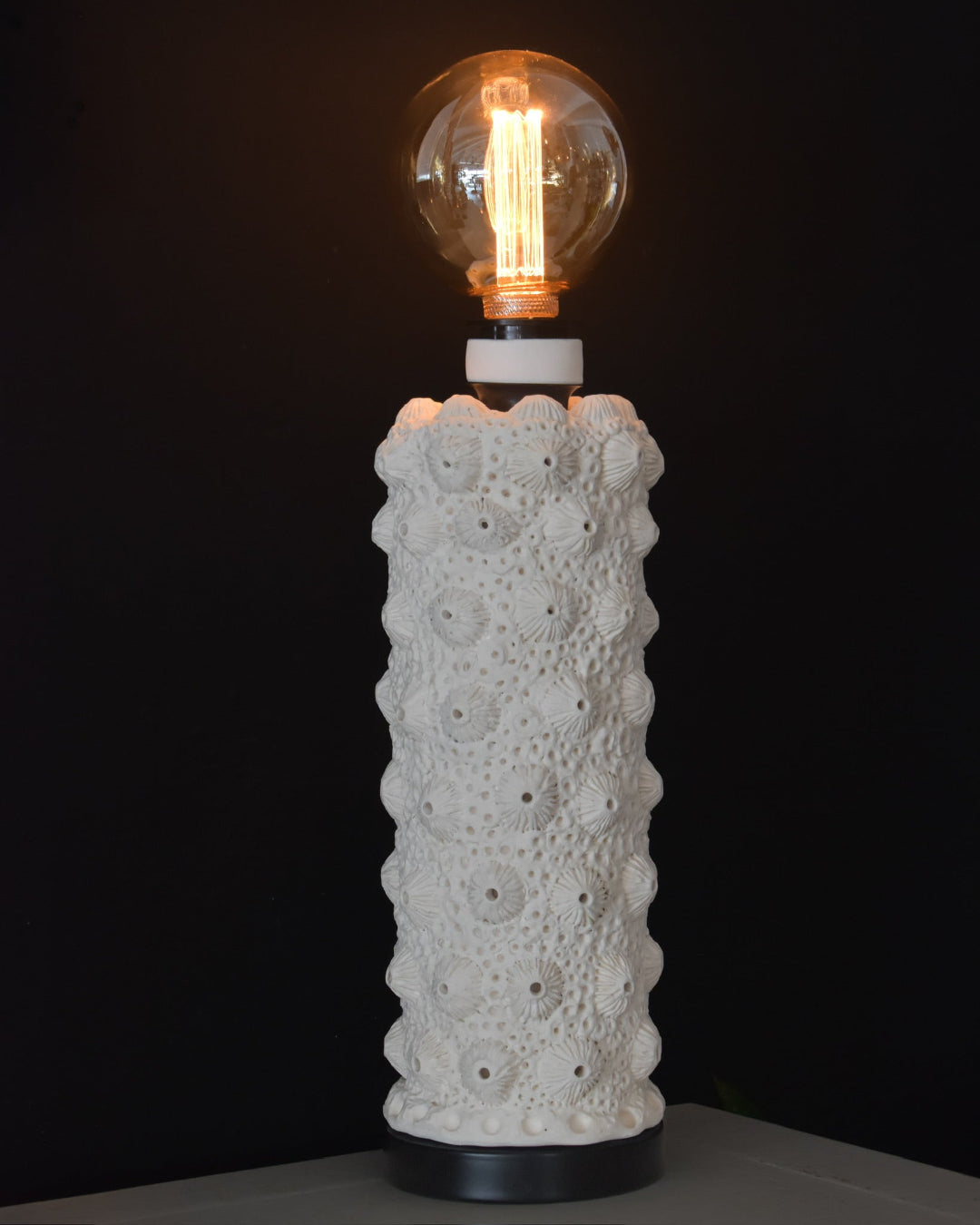 Ceramic table lamp with textured design and lit bulb on a black background