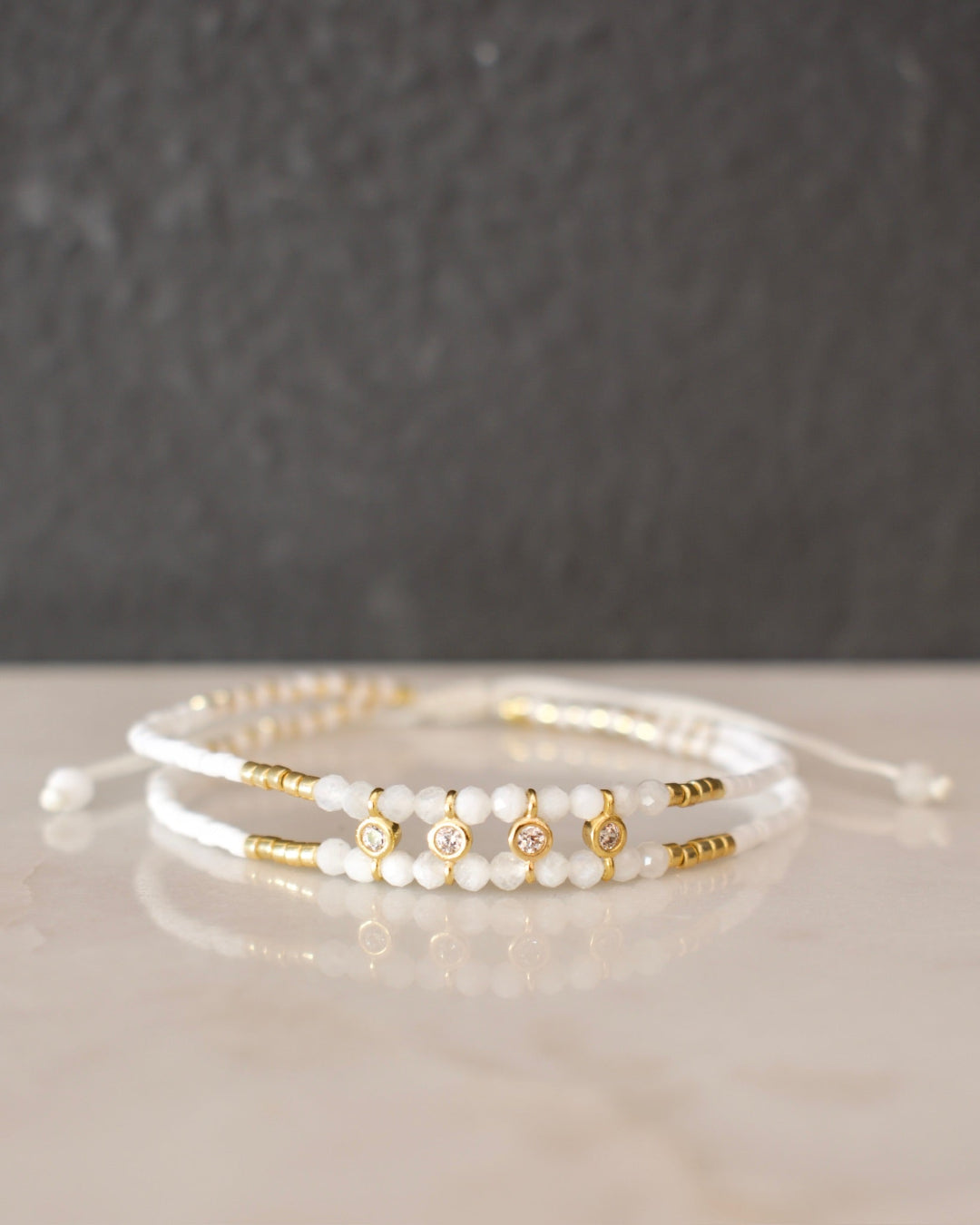 Two pearl and gold beaded bracelets on a neutral background