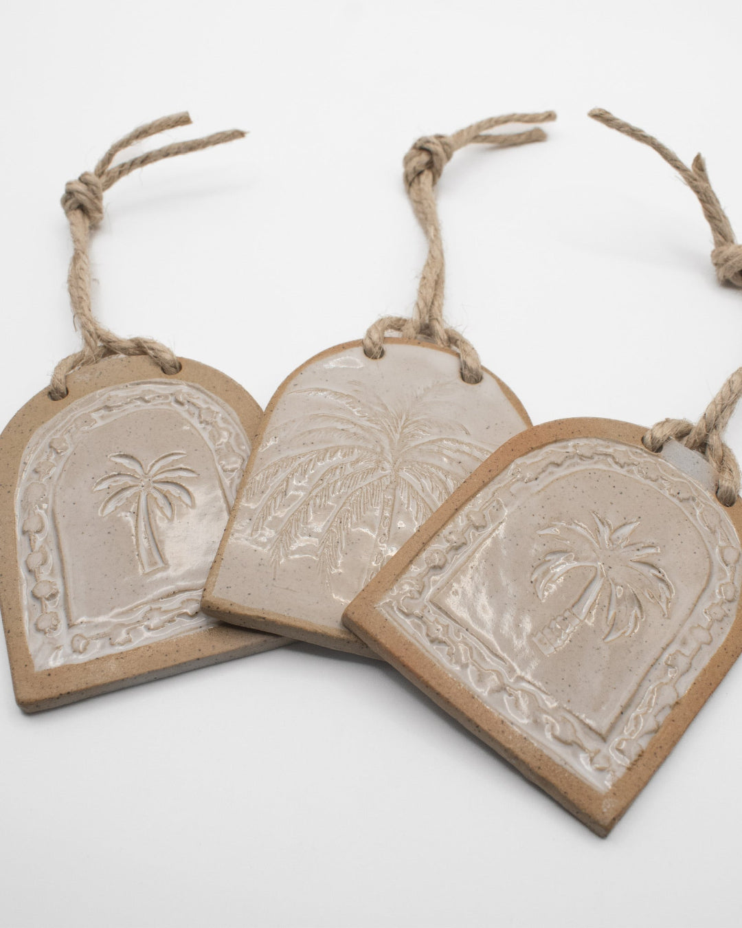Three arched ceramic tags with embossed designs and rope handles on a white background, wedding or engagement gifts