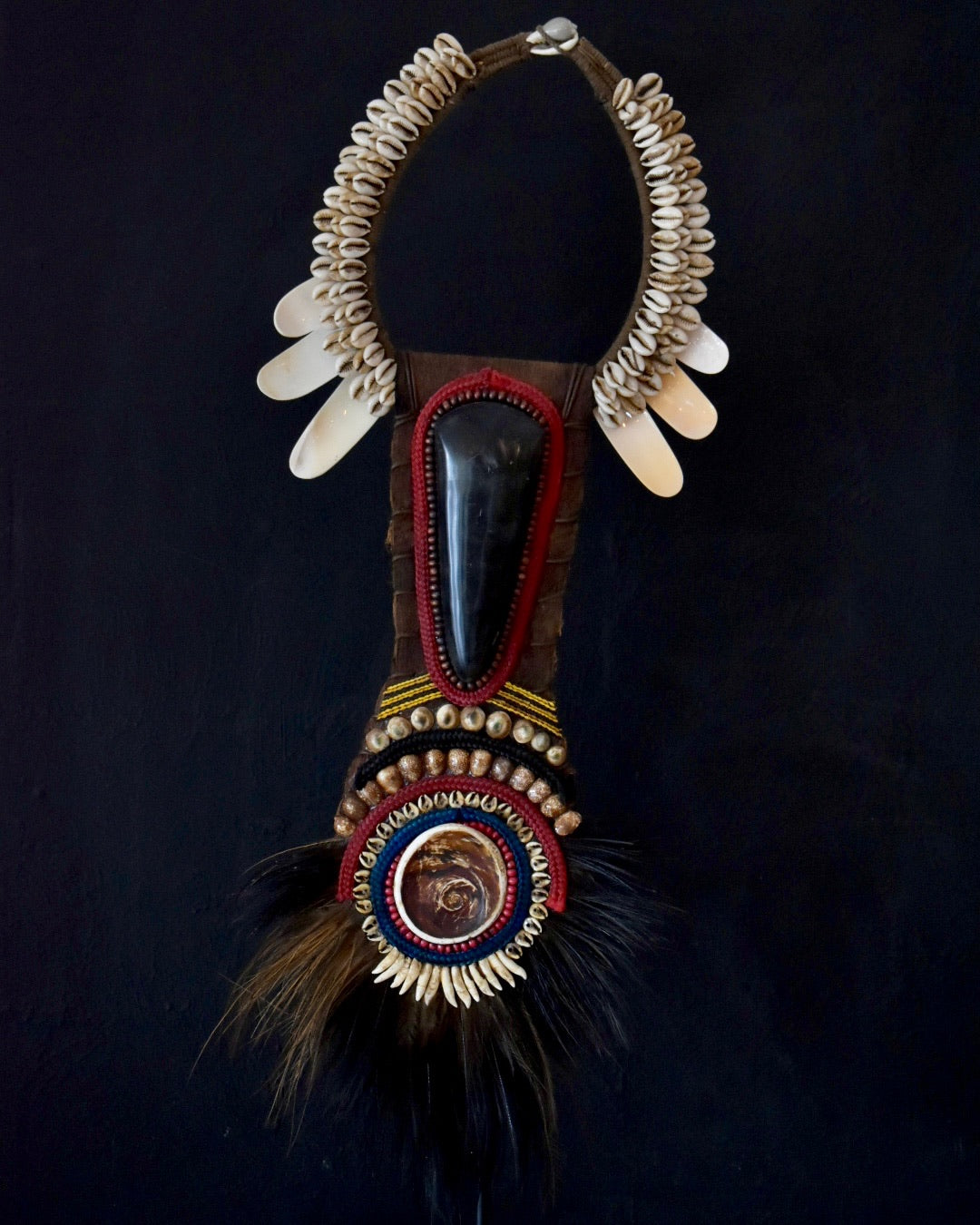 Decorative necklace with bone elements, feathers, and beads on a dark background