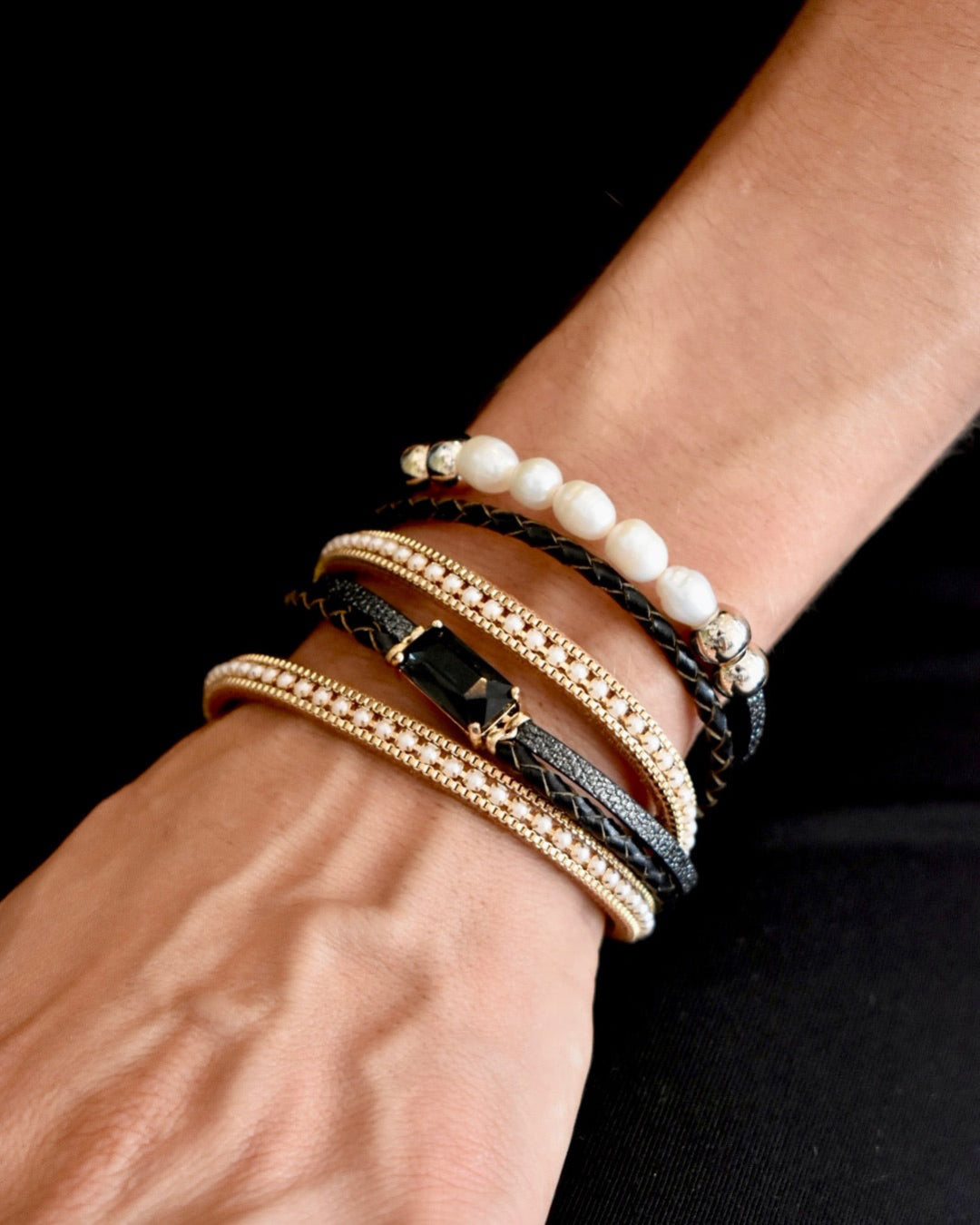 Close-up of a wrist wearing multiple bracelets on a black background