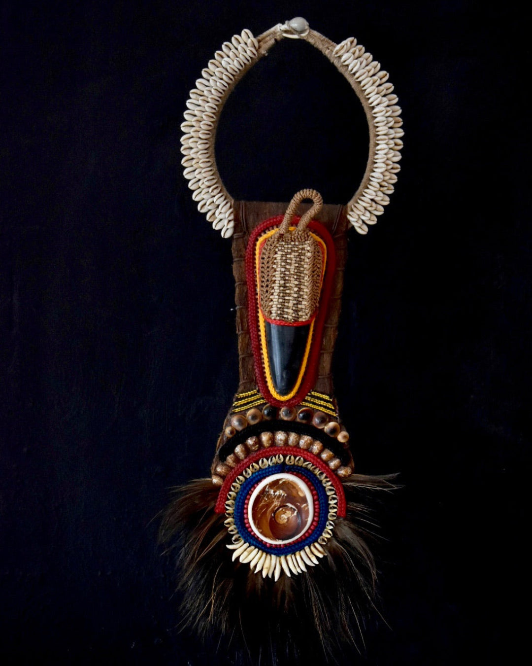 Decorative necklace with intricate designs and feathers on a dark background