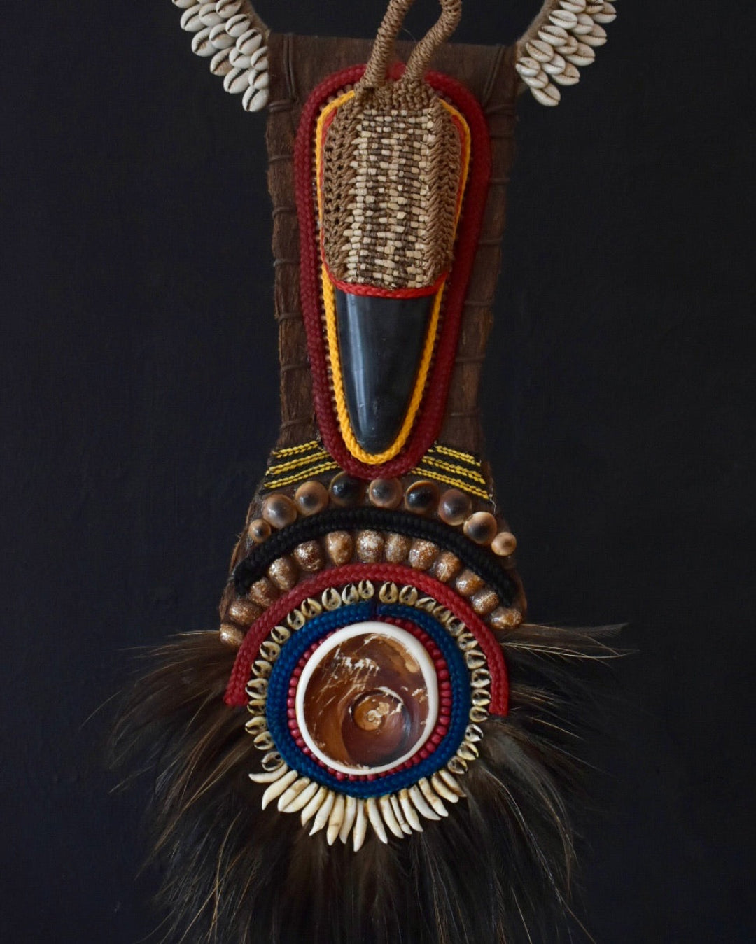 Decorative mask with intricate beadwork and feathers on a dark background