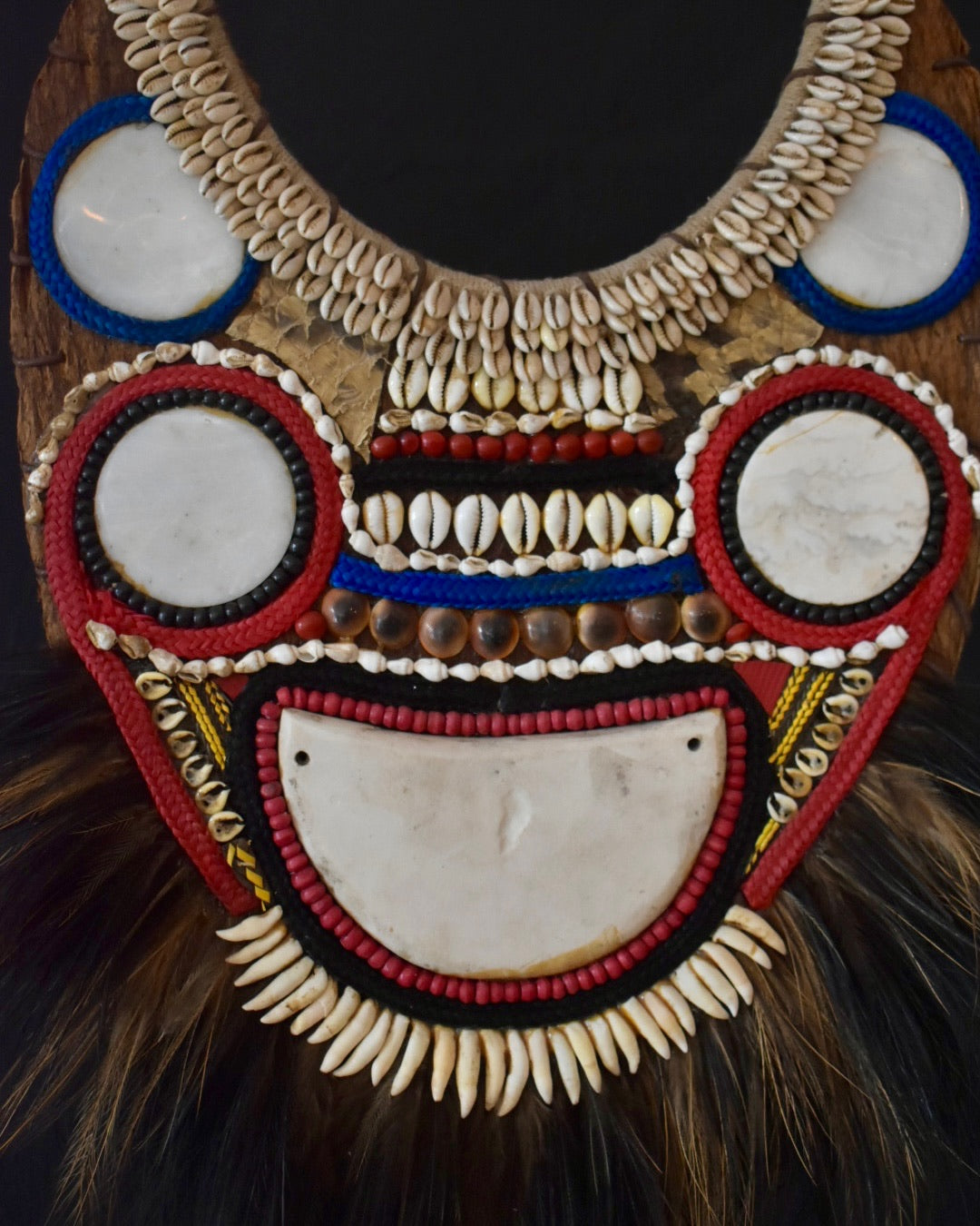 Decorative mask with shell and feather details on a dark background