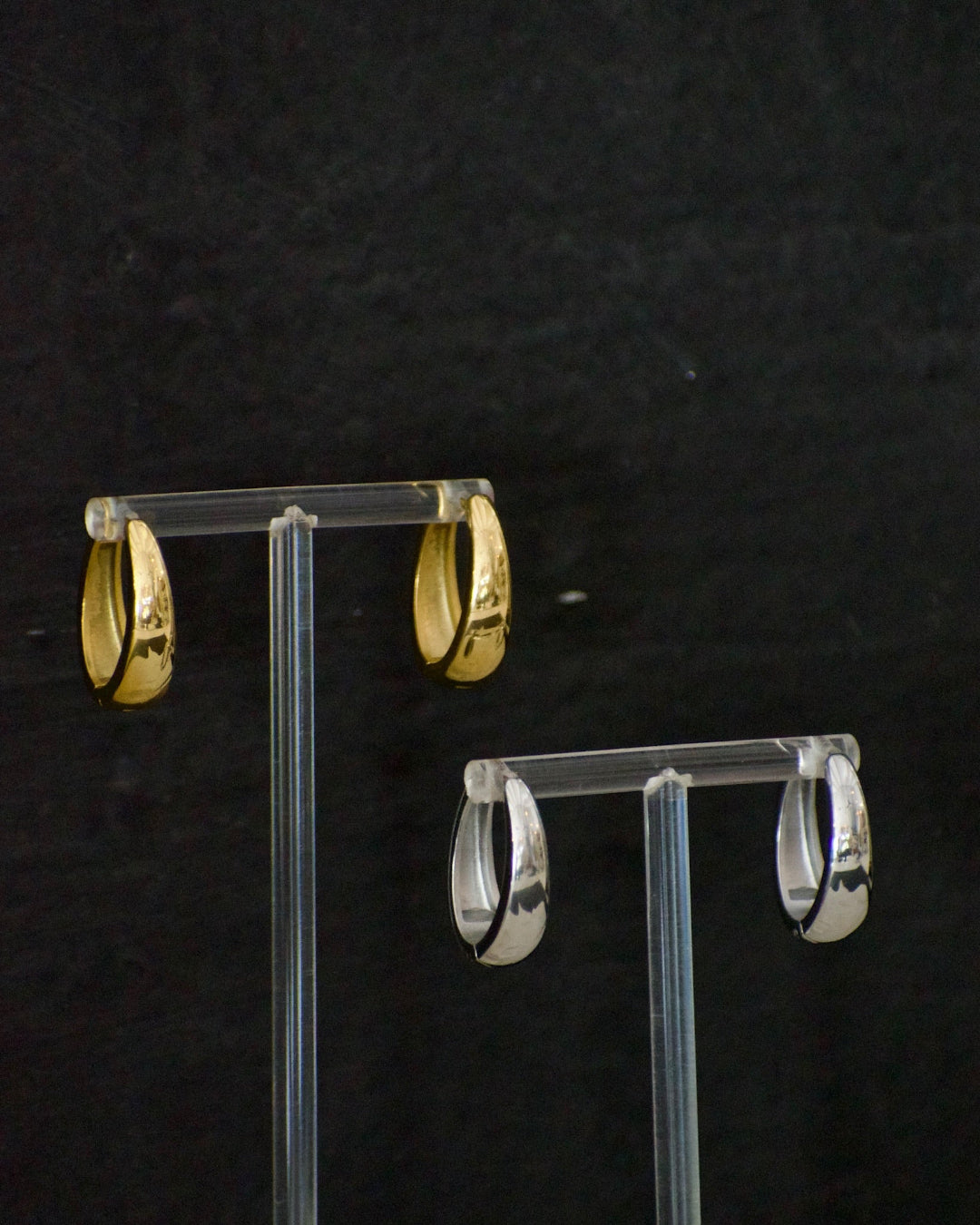 Gold and silver hoop earrings on clear stands against a black background