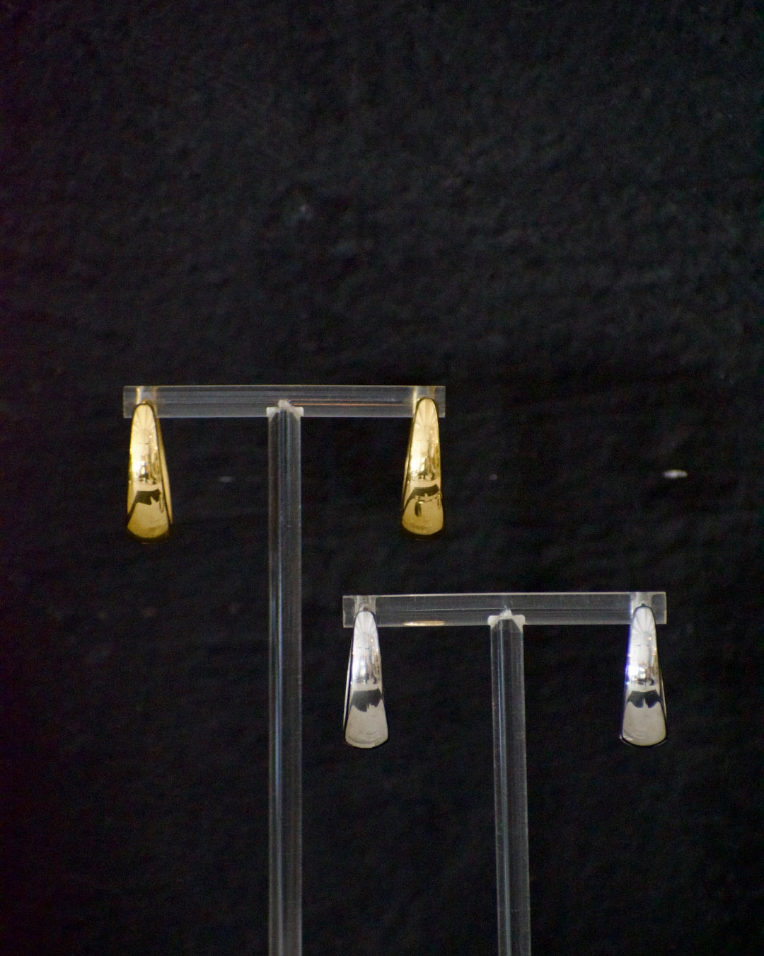 Gold and silver earrings on clear stands against a dark background