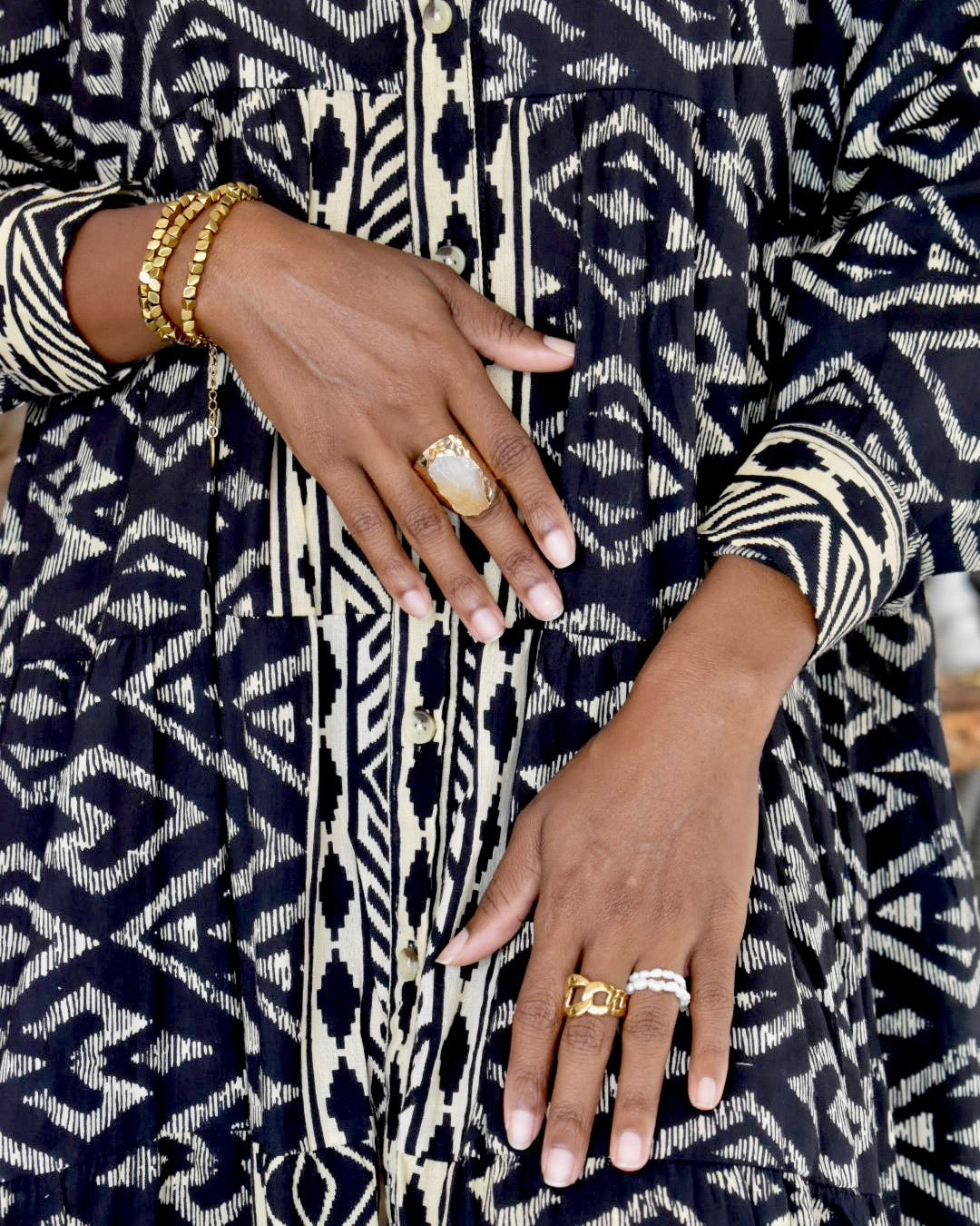 Close-up of a person's hands wearing gold rings and bracelets on a patterned fabric background