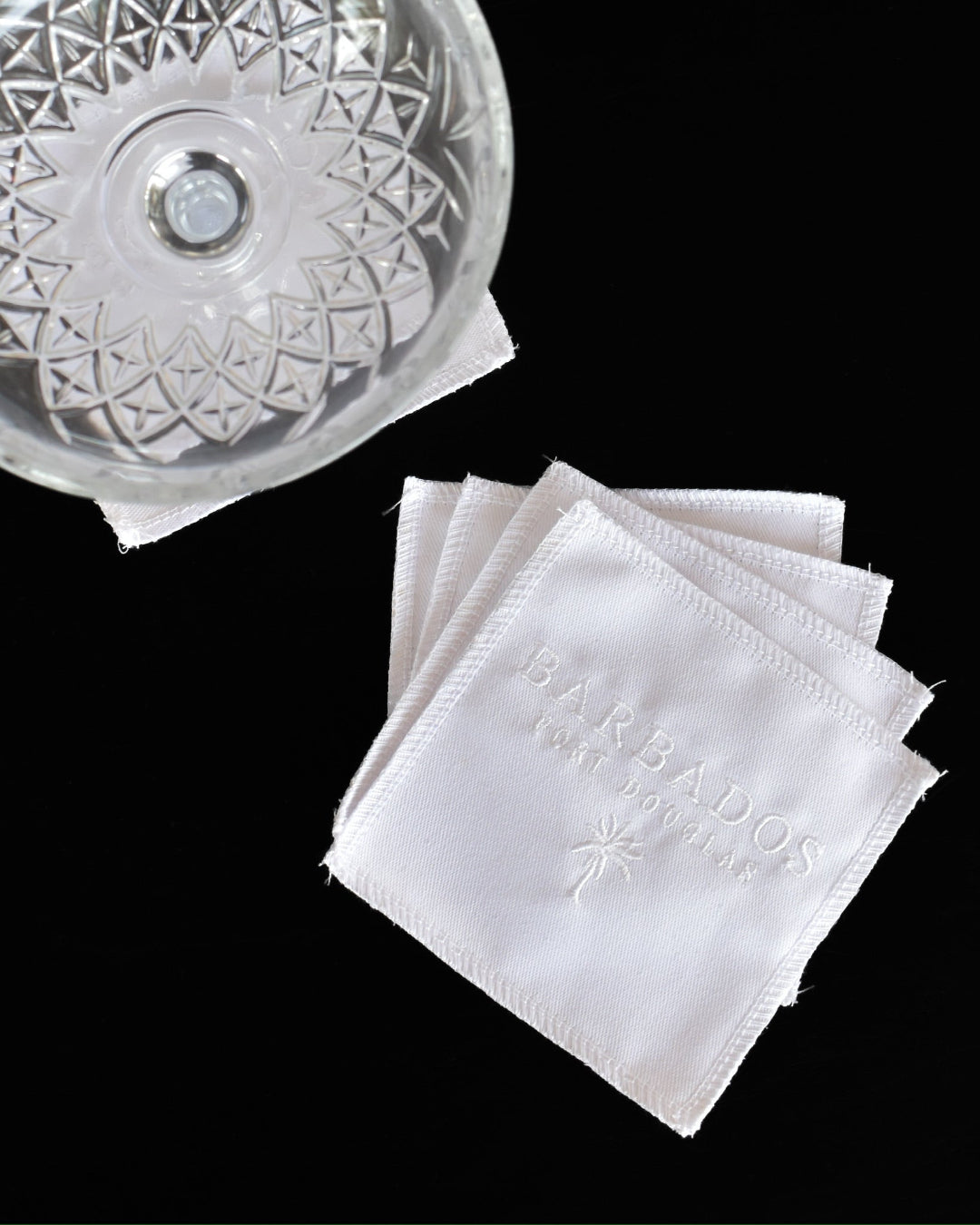 White coasters with 'Barbados Port DOuglas' branding next to a decorative glass bowl on a black background