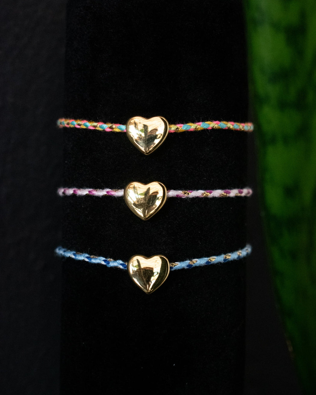 Three gold heart-shaped bracelets on a black surface with a green textured background.