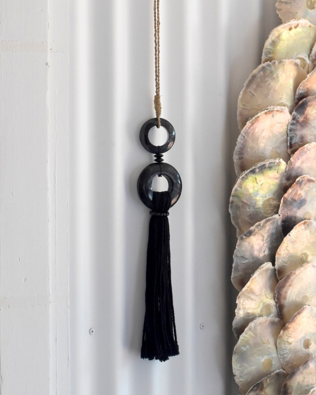 Black tassel hanging against a white wall with a shell decoration in the background