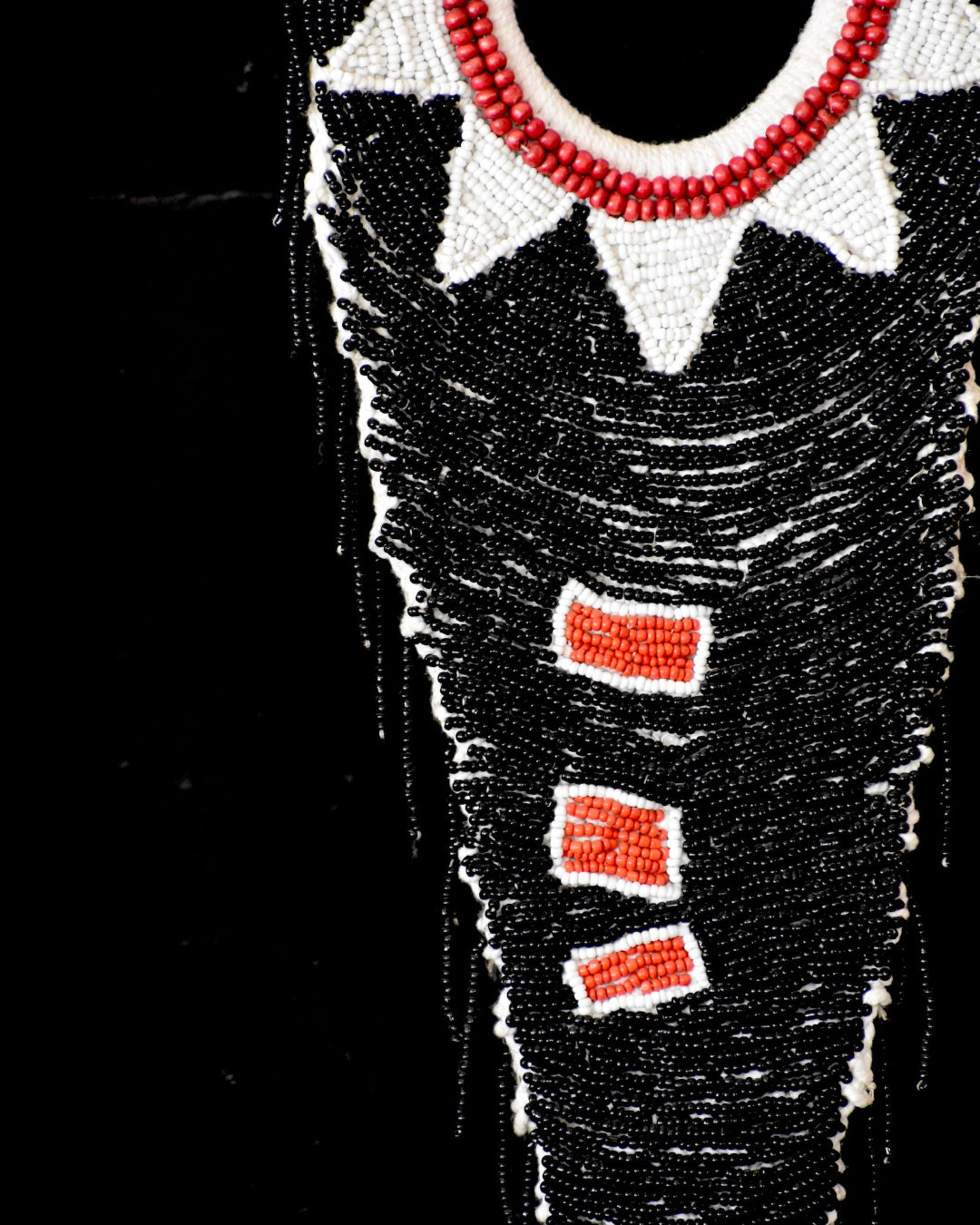 Close-up of a beaded garment with red accents on a black background