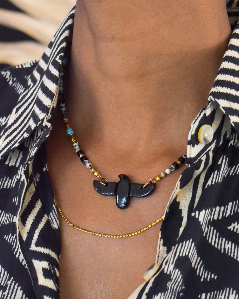 Necklace with a black pendant worn by a person wearing a patterned shirt.