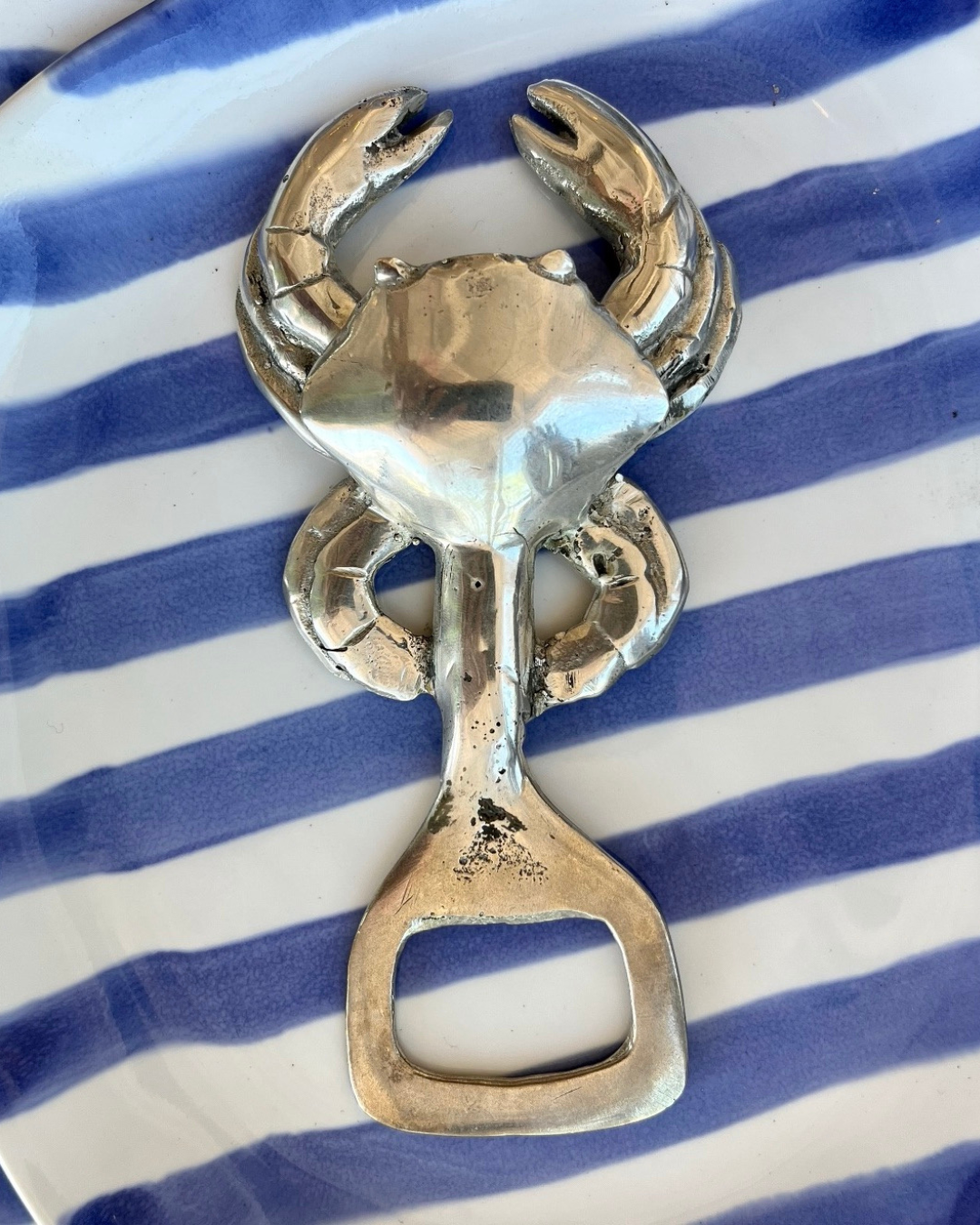 Silver crab-shaped bottle opener on a blue and white striped background