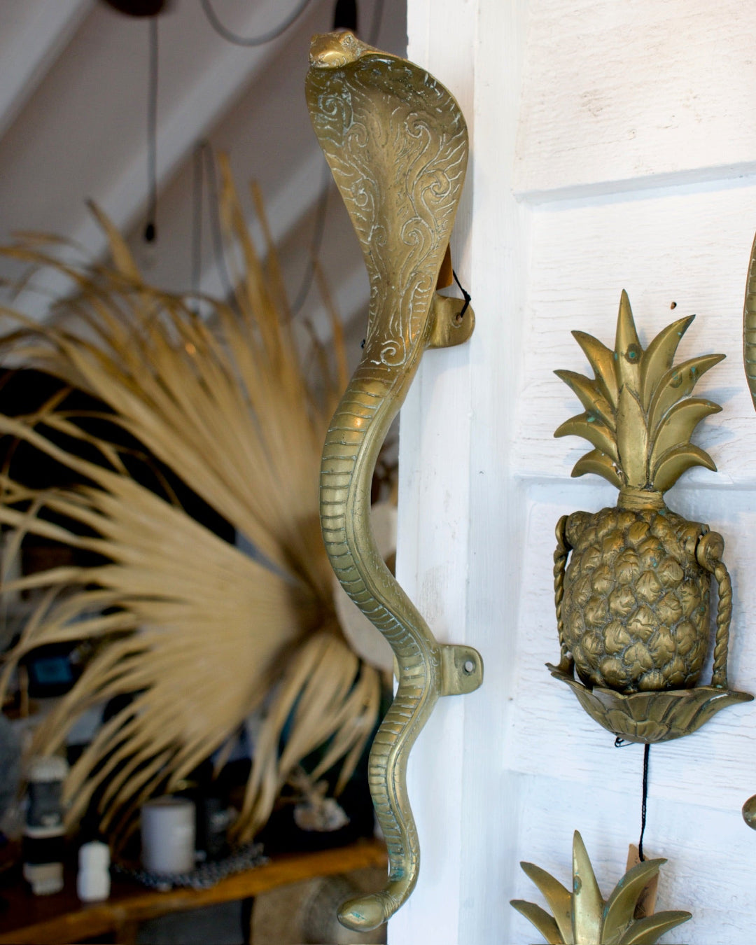 Decorative brass snake and pineapple wall sconces on a white wall.