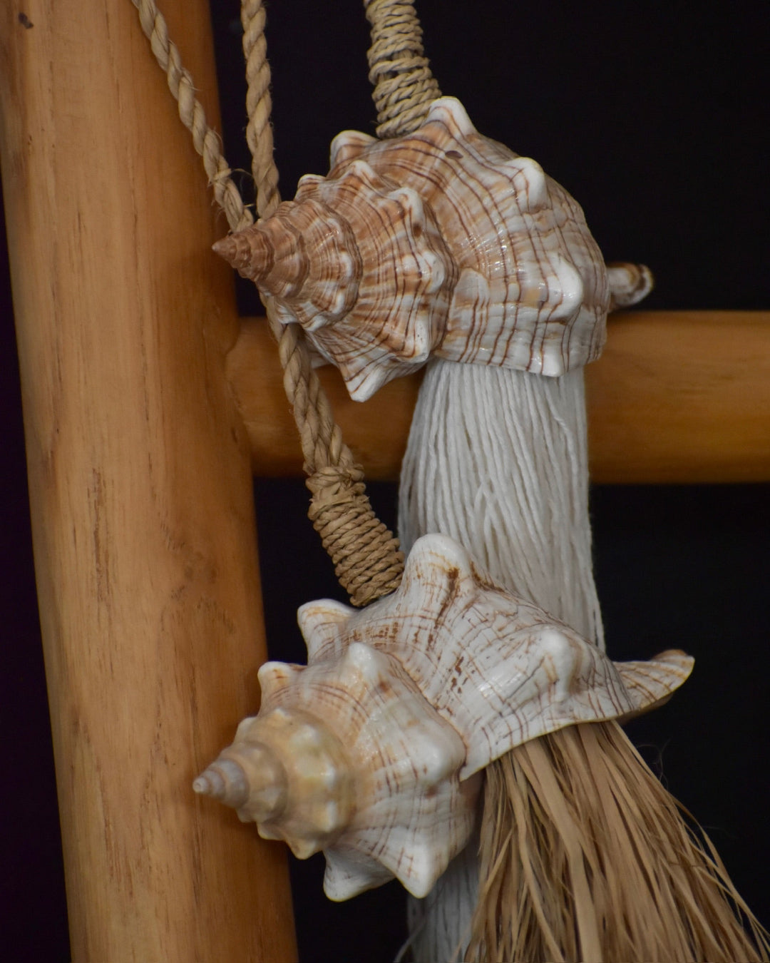 Decorative broom with seashells attached to a wooden handle against a dark background