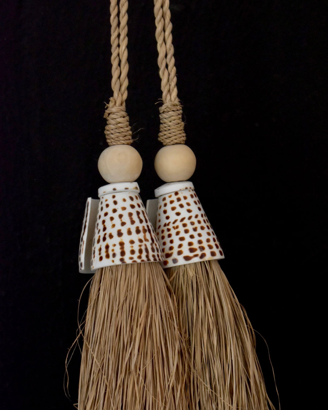 Two decorative tassels with wooden beads and braided strings on a black background