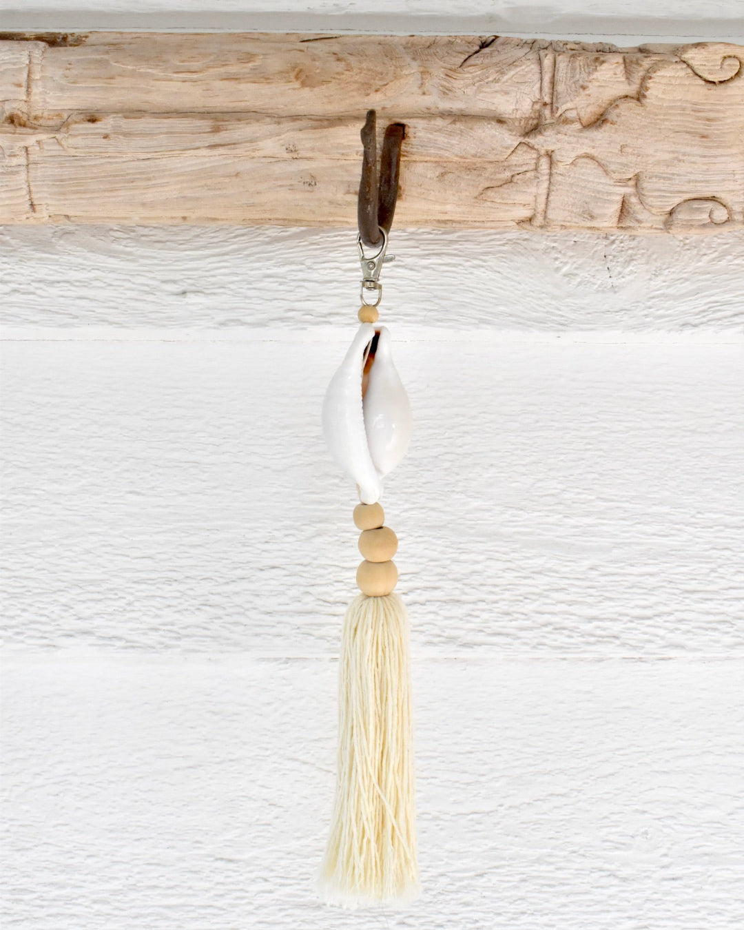 Decorative keychain with a white pendant and beige tassel on a textured white background.