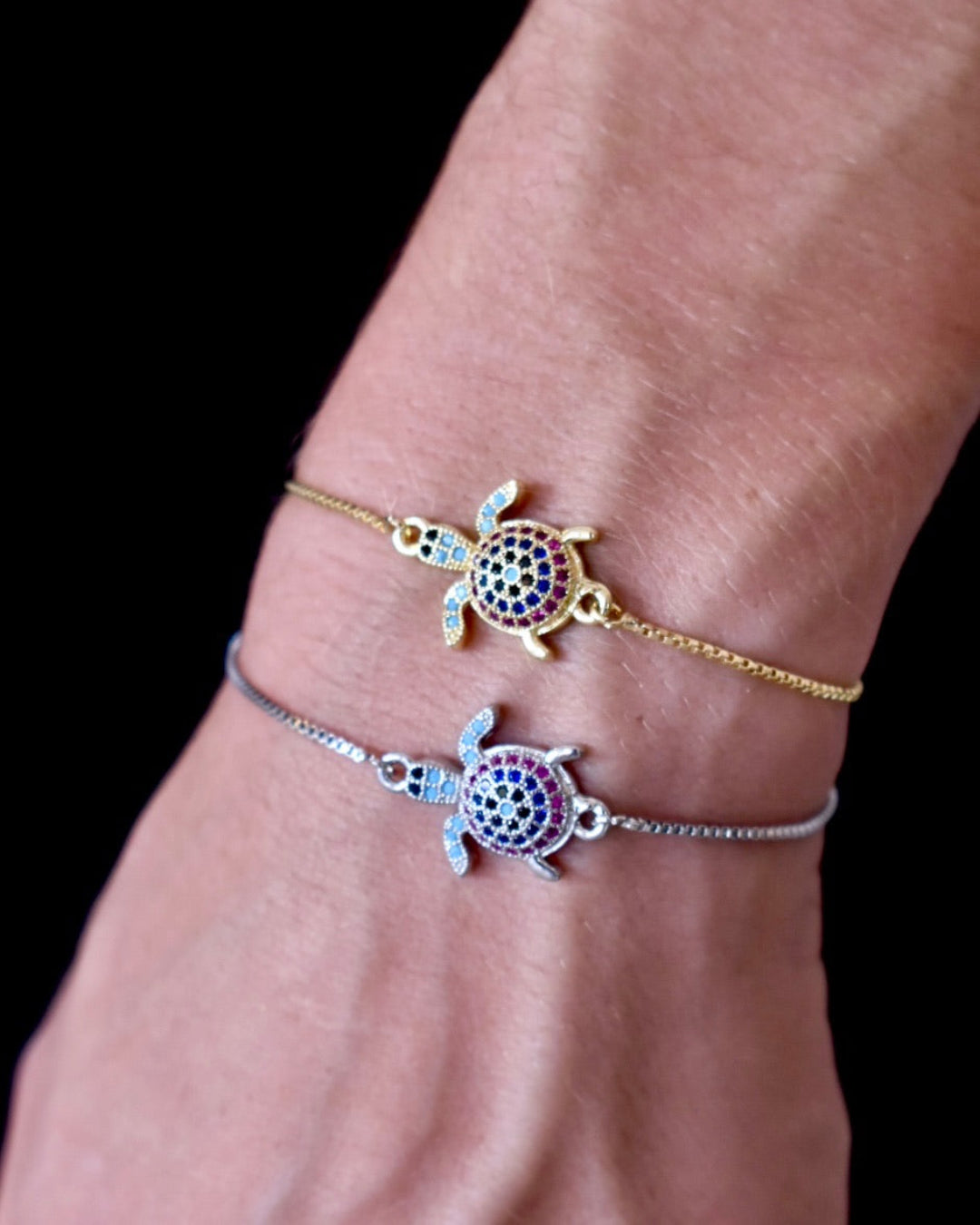 Two turtle-shaped bracelets on a wrist against a black background