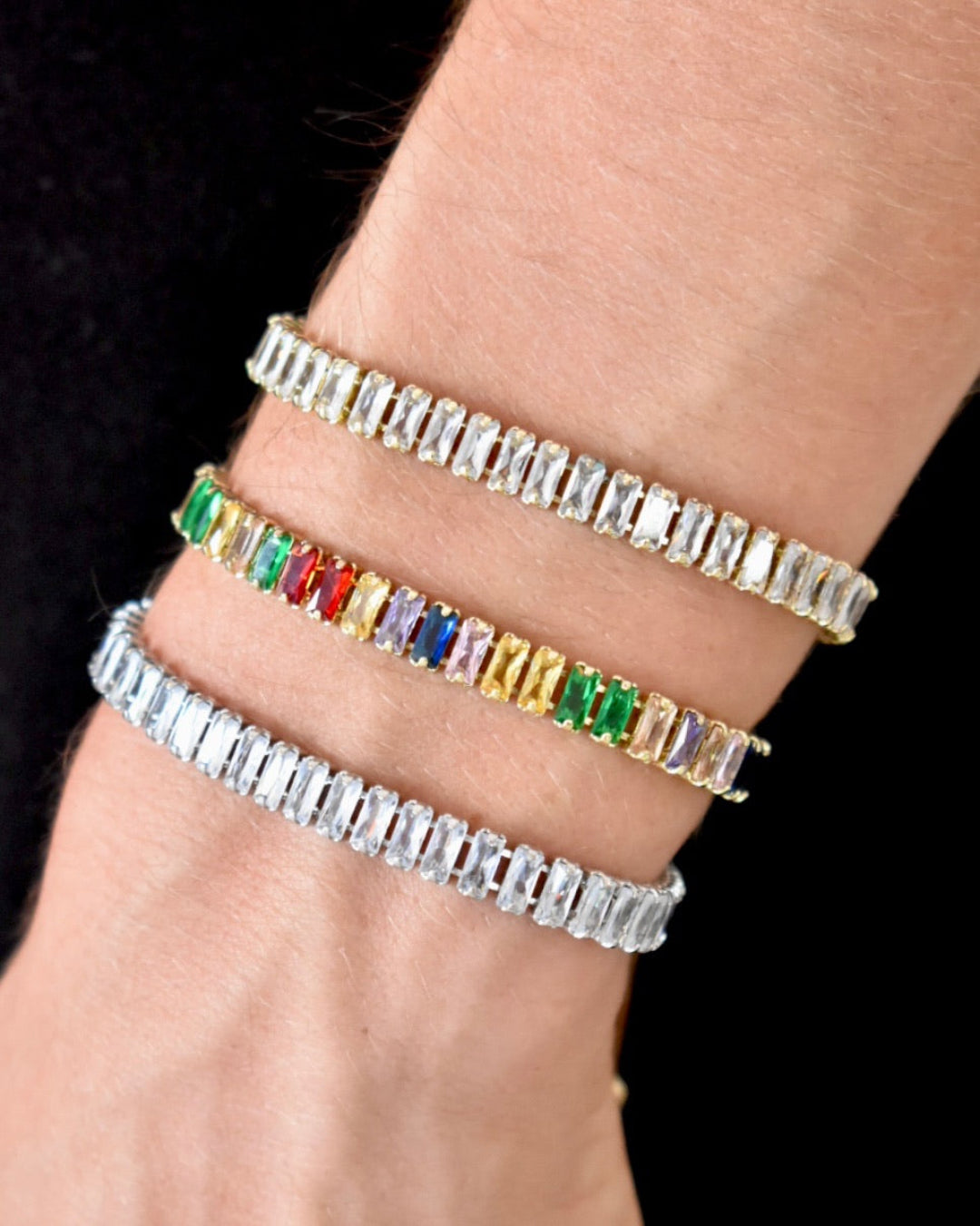 Three colorful gemstone tennis bracelets on a wrist against a black background